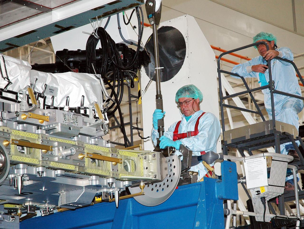 KENNEDY SPACE CENTER, FLA.  - In the Space Station Processing Facility, technician Fred Parisi is attaching the CELA (Cargo Element Lifting Assembly) down rods to the External Stowage Platform -2 (ESP-2) in preparation for lifting the ESP-2 from its transportation container and installing it into the Payload Transportation Canister.  At right, above, is Scott Kisner, task leader.  The ESP-2 will travel to Launch Pad 39B with its fellow payload elements the Lightweight MPESS Carrier (Multi-Purpose Experiment Support Structure) and Multi-Purpose Logistics Module Raffaello in the canister.  Once at the pad, the three payloads will be transferred to the payload bay of Discovery for flight. The ESP-2 is carrying replacement parts to the International Space Station.  The platform will be deployed and attached to the Station’s airlock and used as a permanent spare parts facility.  STS-114 is targeted for launch during a window that extends from May 15 through June 3.