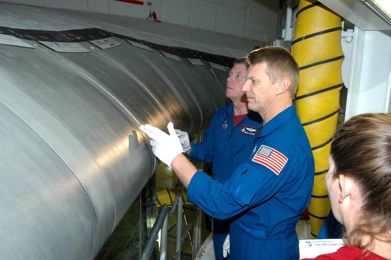 KENNEDY SPACE CENTER, FLA. - In the Orbiter Processing Facility, STS-121 Mission Specialists Michael E. Fossum (left) and Piers J. Sellers receive a briefing and up-close look at the wing leading edge of Space Shuttle Atlantis, the orbiter that will take them into space. The leading edge of each of the orbiters’ wings has 22 Reinforced Carbon-Carbon panels, made entirely of carbon composite material.  The molded components are approximately 0.25-inch to 0.5-inch thick. The astronauts of the second Return to Flight mission, STS-121, are at Kennedy Space Center to participate in the Crew Equipment Interface Test (CEIT). During CEIT, the crew has an opportunity to get a hands-on look at the orbiter and equipment they will be working with on their mission. Mission STS-121 is scheduled to launch in July.