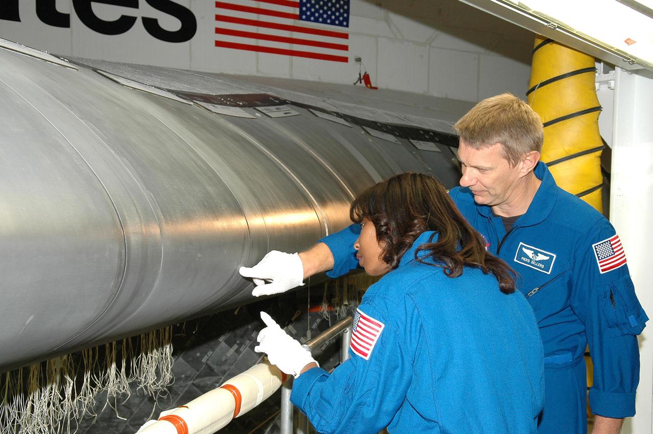 KENNEDY SPACE CENTER, FLA. - In the Orbiter Processing Facility, STS-121 Mission Specialists Stephanie D. Wilson (left) and Piers J. Sellers receive a briefing and up-close look at the wing leading edge of Space Shuttle Atlantis, the orbiter that will take them into space. The leading edge of each of the orbiters’ wings has 22 Reinforced Carbon-Carbon panels, made entirely of carbon composite material. The molded components are approximately 0.25-inch to 0.5-inch thick. The astronauts of the second Return to Flight mission, STS-121, are at Kennedy Space Center to participate in the Crew Equipment Interface Test (CEIT). During CEIT, the crew has an opportunity to get a hands-on look at the orbiter and equipment they will be working with on their mission. Mission STS-121 is scheduled to launch in July.