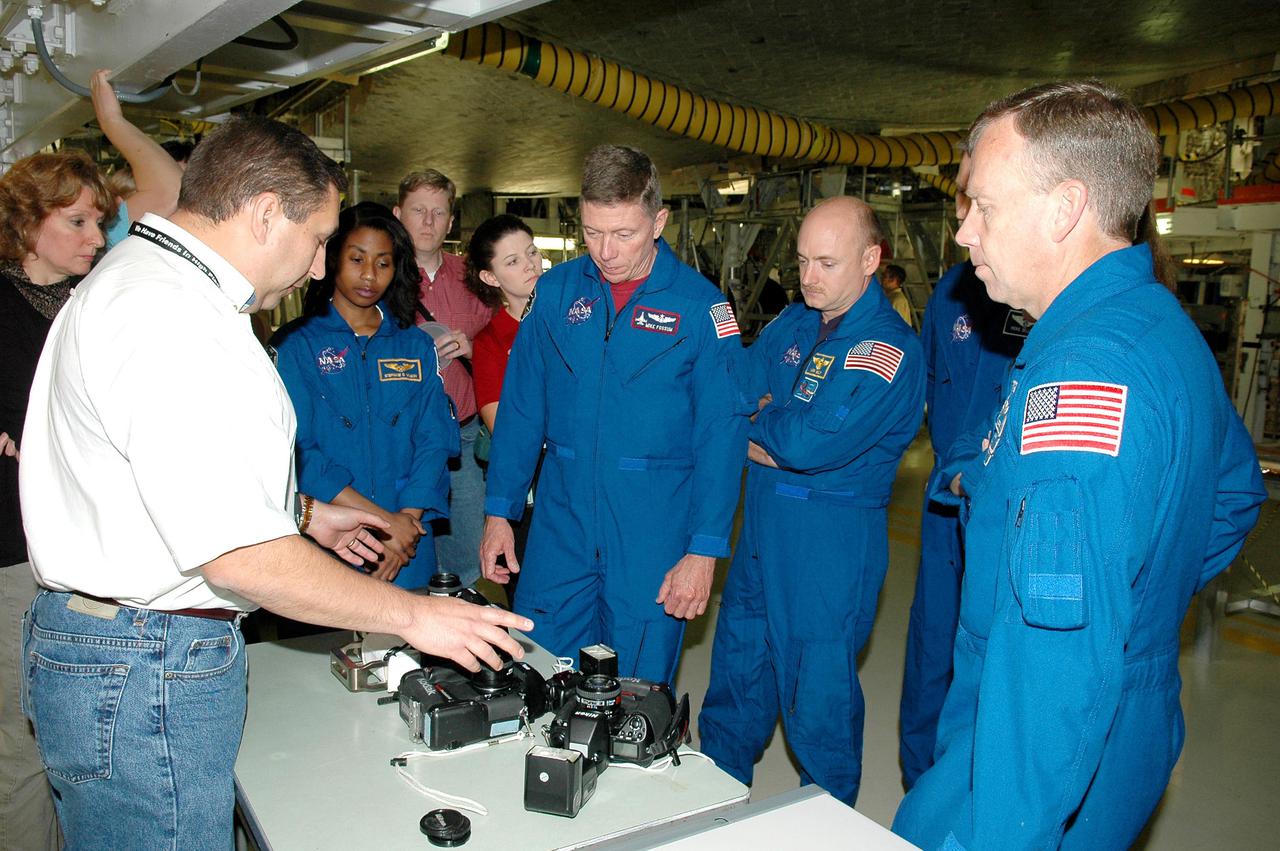 KENNEDY SPACE CENTER, FLA. - In the Orbiter Processing Facility, the STS-121 crew receives a briefing and up-close look beneath Space Shuttle Atlantis at the handheld cameras they will carry into space. From left, in the blue flight suits, are Mission Specialists Stephanie D. Wilson and Michael E. Fossum, Pilot Mark E. Kelly and Commander Steven W. Lindsey. The astronauts of the second Return to Flight mission, STS-121, are at Kennedy Space Center to participate in the Crew Equipment Interface Test (CEIT). During CEIT, the crew has an opportunity to get a hands-on look at the orbiter and equipment they will be working with on their mission. Mission STS-121 is scheduled to launch in July.