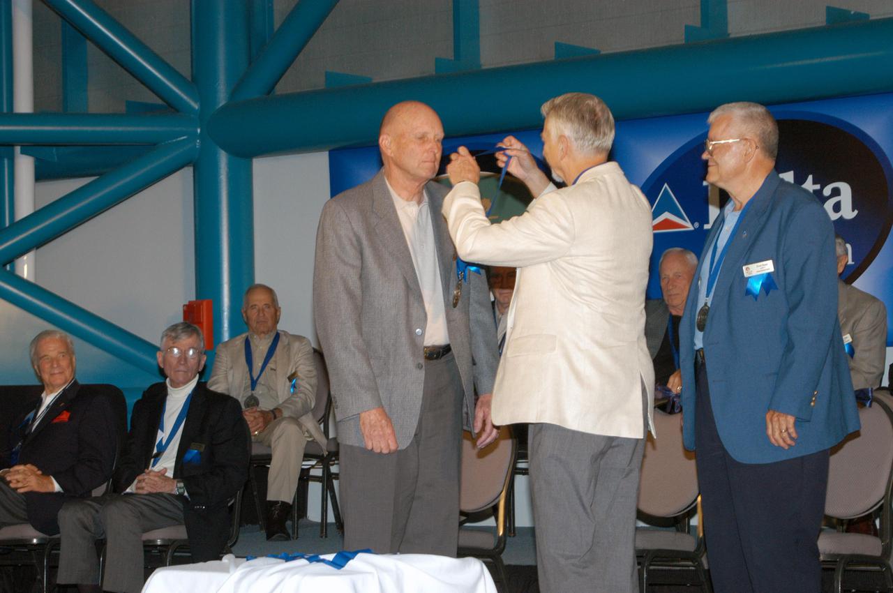 KENNEDY SPACE CENTER, FLA. -  At the Astronaut Hall of Fame Induction Ceremony, Chairman Owen Garriott (center) places a medal around the neck of new inductee Gordon Fullerton.  At right is Hall of Famer Fred Haise.  Other Hall of Famers are gathered on stage for the ceremony, which is being held in the Kennedy Space Center Visitor Complex’s Apollo_Saturn V Center.  Recognized for their individual flight accomplishments and contributions to the success and future success of the U.S. space program, this elite group of inductees is among only 60 astronauts to be honored in the Hall of Fame and the fourth group of Space Shuttle astronauts named.