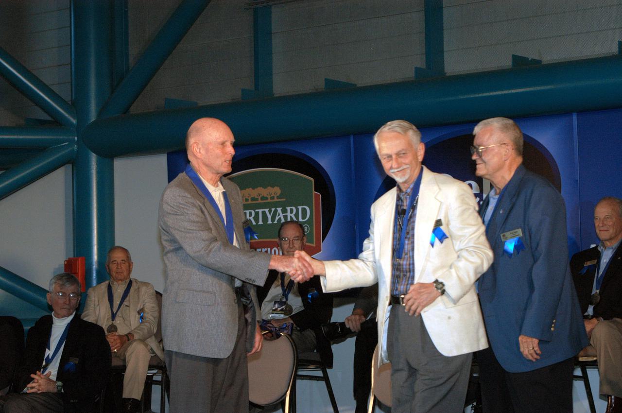 KENNEDY SPACE CENTER, FLA. -  At the Astronaut Hall of Fame Induction Ceremony, new inductee Gordon Fullerton (left) is congratulated by Chairman Owen Garriott.  At right is Hall of Famer Fred Haise. Other Hall of Famers are gathered on stage for the ceremony, which is being held in the Kennedy Space Center Visitor Complex’s Apollo_Saturn V Center.  Recognized for their individual flight accomplishments and contributions to the success and future success of the U.S. space program, this elite group of inductees is among only 60 astronauts to be honored in the Hall of Fame and the fourth group of Space Shuttle astronauts named.