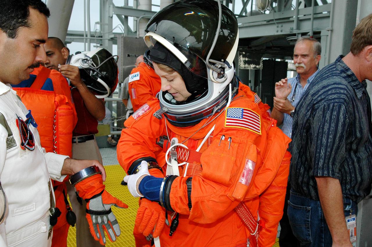 KENNEDY SPACE CENTER, FLA. - Following the mock countdown on Launch Pad 39B, STS-114 Commander Eileen Collins (center) adjusts her glove before climbing into a slidewire basket used for emergency egress from the Fixed Service Structure at the pad. This is part of the pre-launch training included in Terminal Countdown Demonstration Test (TCDT) activities. TCDT provides the crew of each mission an opportunity to participate in various simulated countdown activities, including equipment familiarization and emergency egress training. STS-114 is the first Return to Flight mission to the International Space Station. The launch window extends July 13 through July 31.