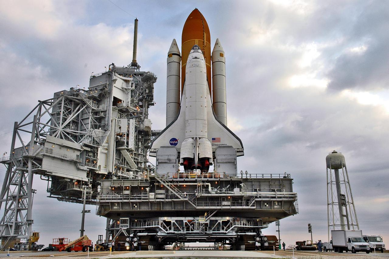KENNEDY SPACE CENTER, FLA.  -  Under post-dawn cloudy skies, Space Shuttle Discovery, resting on the Mobile Launcher Platform, begins rolling off Launch Pad 39B via the Crawler_Transporter underneath.  At left are the Rotating and Fixed Service Structures (RSS and FSS).  The 80-foot lightning mast is atop the FSS. At right is the  290-foot-tall water tower that holds 300,000 gallons of water, part of the sound suppression system during a launch.  Discovery is returning to the Vehicle Assembly Buildling where it will be demated from its External Tank and lifted into the transfer aisle.  On or about June 7, Discovery will be lifted and attached to its new tank and Solid Rocket Boosters, which are already in the VAB.  Only the 15th rollback in Space Shuttle Program history, the 4.2-mile journey allows additional modifications to be made to the External Tank prior to a safe Return to Flight.  Discovery is expected to be rolled back to the launch pad in mid-June for Return to Flight mission STS-114.  The launch window extends from July 13 to July 31.