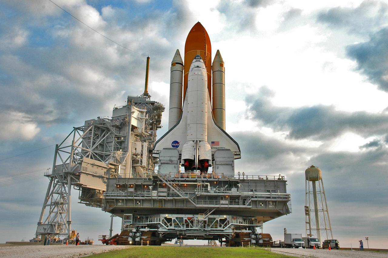 KENNEDY SPACE CENTER, FLA.  -  Under post-dawn cloudy skies, Space Shuttle Discovery, resting on the Mobile Launcher Platform, rolls away from Launch Pad 39B via the Crawler_Transporter underneath.  At left are the Rotating and Fixed Service Structures (RSS and FSS).  Atop the FSS is the 80-foot lightning mast. At right is the  290-foot-tall water tower that holds 300,000 gallons of water, part of the sound suppression system during a launch.  Discovery is returning to the Vehicle Assembly Buildling where it will be demated from its External Tank and lifted into the transfer aisle.  On or about June 7, Discovery will be lifted and attached to its new tank and Solid Rocket Boosters, which are already in the VAB.  Only the 15th rollback in Space Shuttle Program history, the 4.2-mile journey allows additional modifications to be made to the External Tank prior to a safe Return to Flight.  Discovery is expected to be rolled back to the launch pad in mid-June for Return to Flight mission STS-114.  The launch window extends from July 13 to July 31.