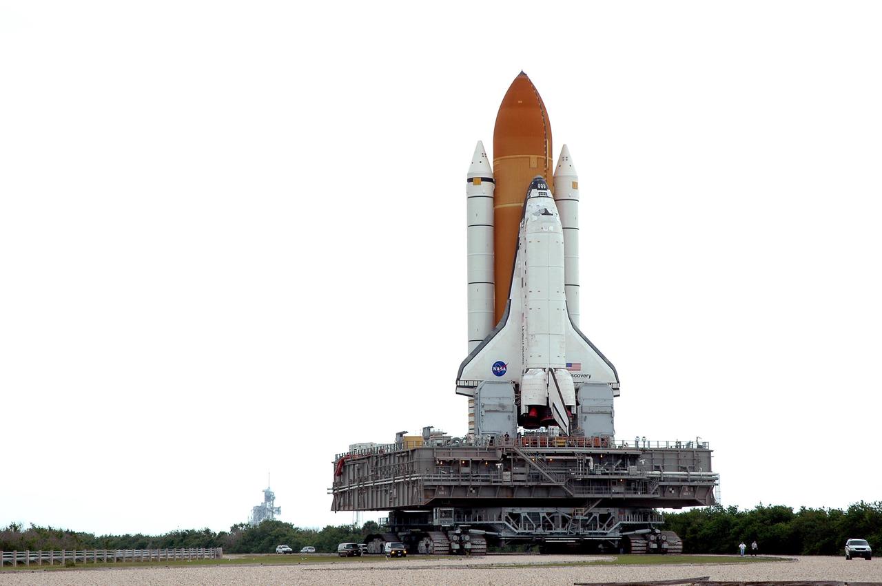 KENNEDY SPACE CENTER, FLA. - Dwarfing the accompanying vehicles, Space Shuttle Discovery, resting on the Mobile Launcher Platform atop the Crawler_Transporter, heads along the crawlerway to the Vehicle Assembly Building (VAB). Discovery is rolling back from Launch Pad 39B (in the background). Once inside the VAB, Discovery will be demated from its External Tank and lifted into the transfer aisle. On or about June 7, Discovery will be lifted and attached to its new tank and Solid Rocket Boosters, which are already in the VAB. Only the 15th rollback in Space Shuttle Program history, the 4.2-mile journey allows additional modifications to be made to the External Tank prior to a safe Return to Flight. Discovery is expected to be rolled back to the launch pad in mid-June for Return to Flight mission STS-114. The launch window extends from July 13 to July 31.