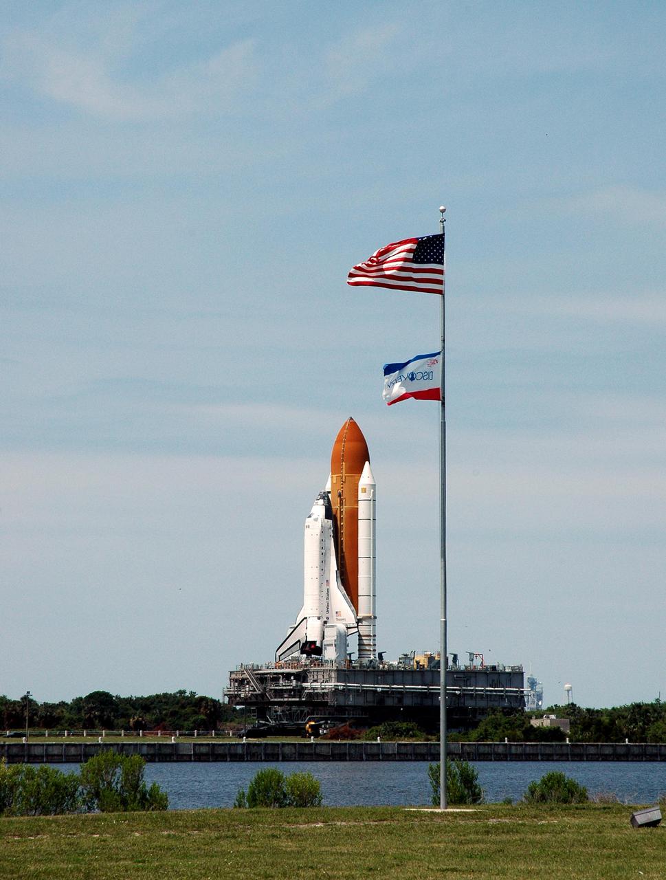 KENNEDY SPACE CENTER, FLA.  -  Space Shuttle Discovery, atop its Mobile Launcher Platform and Crawler_Transporter, inches its way back to NASA’s Vehicle Assembly Building (VAB) at Kennedy Space Center.  Rolling back from Launch Pad 39B, it is passing alongside the turn basin near the VAB and the flag pole that is located near the NASA News Center. Once inside the VAB, Discovery will be demated from its External Tank and lifted into the transfer aisle.  On or about June 7, Discovery will be lifted and attached to its new tank and Solid Rocket Boosters, which are already in the VAB.  Only the 15th rollback in Space Shuttle Program history, the 4.2-mile journey allows additional modifications to be made to the External Tank prior to a safe Return to Flight.  Discovery is expected to be rolled back to the launch pad in mid-June for Return to Flight mission STS-114.  The launch window extends from July 13 to July 31.