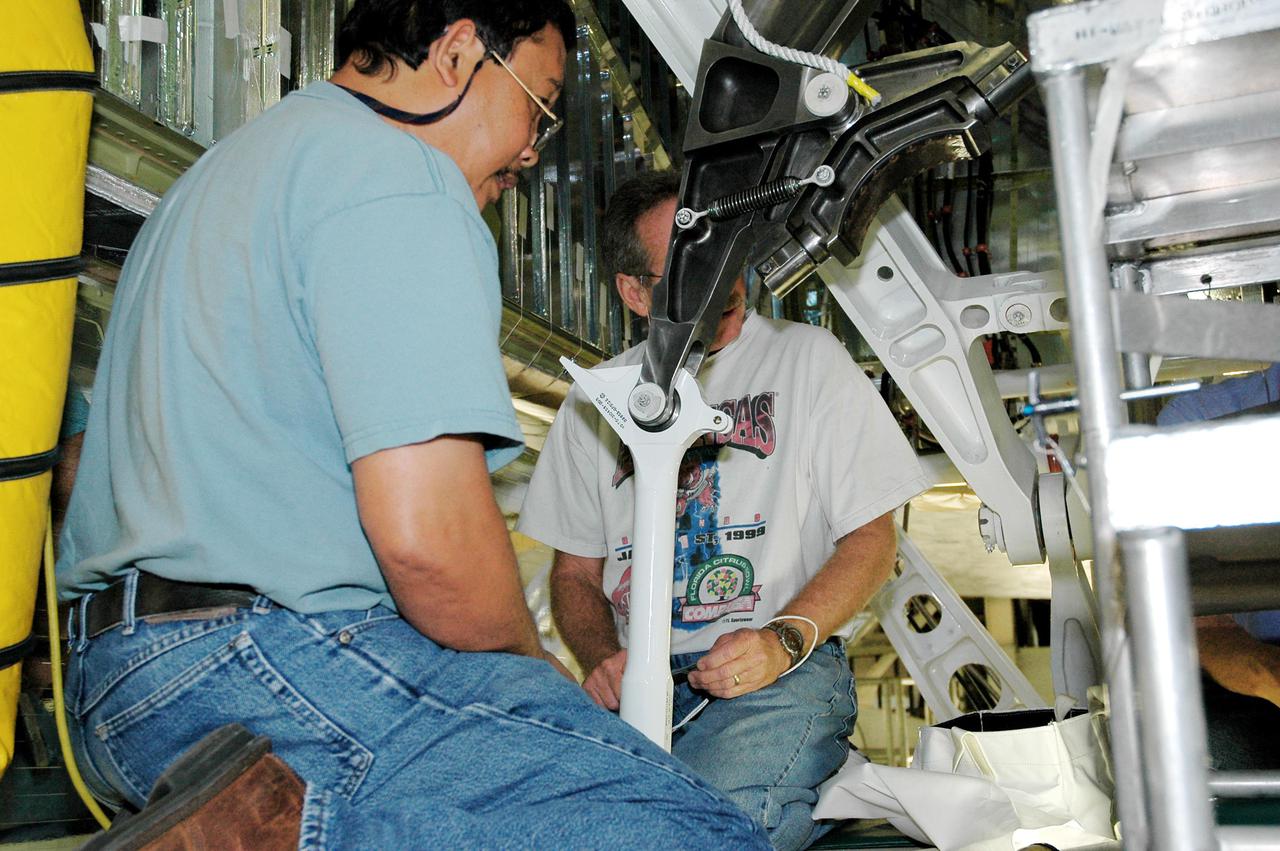 KENNEDY SPACE CENTER, FLA.  -  Inside the wheel well behind Atlantis’ right-hand main landing gear, workers attaches one end of a retract link.  It replaces one in which a small crack was recently found.  To lower the main landing gear, a mechanical linkage released by each gear actuates the doors to the open position.  The landing gear reach the full-down and extended position with 10 seconds and are locked in the down position by spring-loaded downlock bungees  Atlantis is scheduled to launch in September 2005 on the second Return to Flight mission, STS-121.