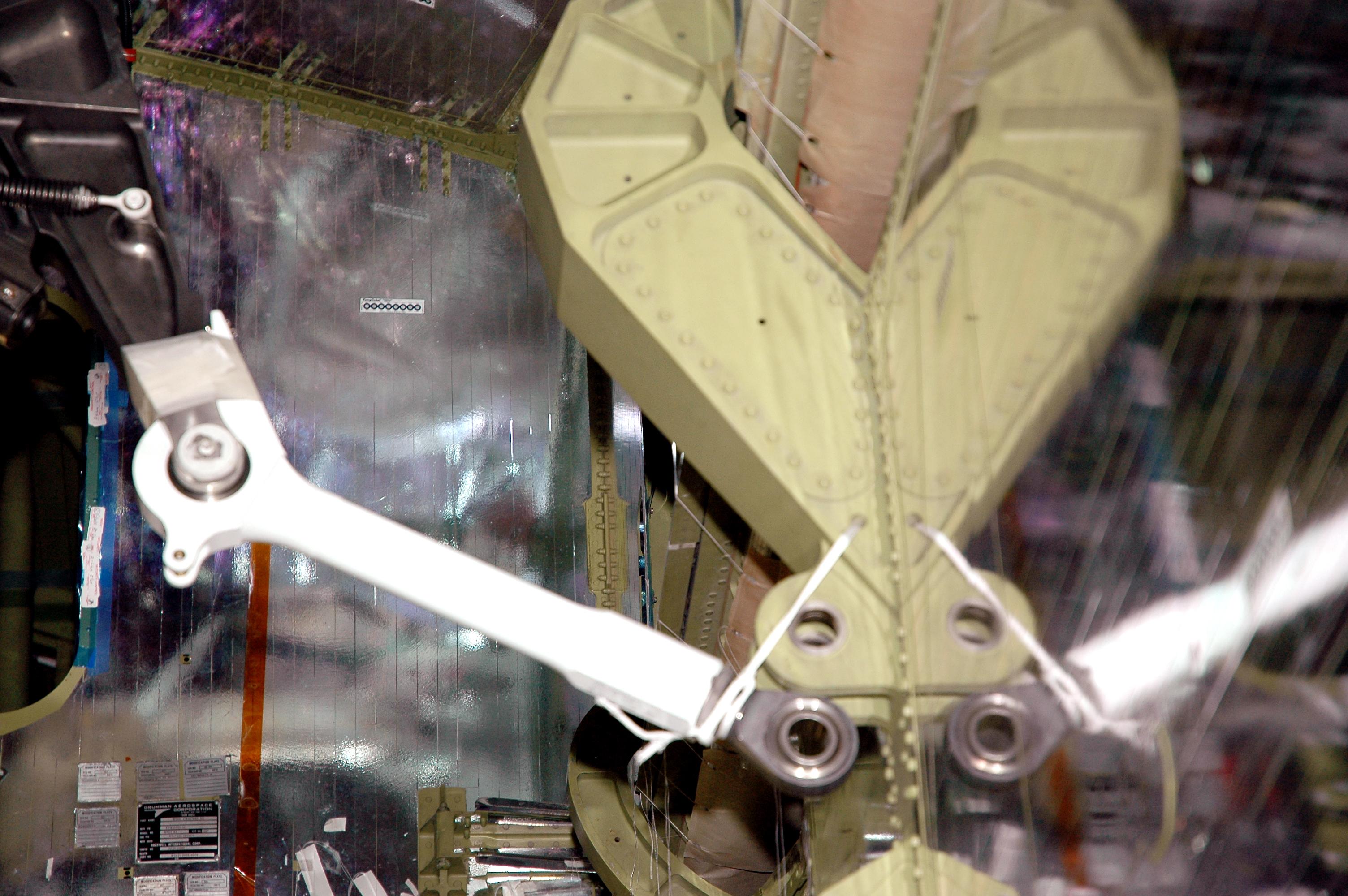 KENNEDY SPACE CENTER, FLA. - In the Orbiter Processing Facility at NASA’s Kennedy Space Center, a replacement retract link (left) is being installed because a small crack was found recently on the retract link assembly. One end of the link is tethered until it is attached. At right is a blurred reflection on a plastic barrier. To lower the main landing gear, a mechanical linkage released by each gear actuates the doors to the open position. The landing gear reach the full-down and extended position with 10 seconds and are locked in the down position by spring-loaded downlock bungees Atlantis is scheduled to launch in September 2005 on the second Return to Flight mission, STS-121.