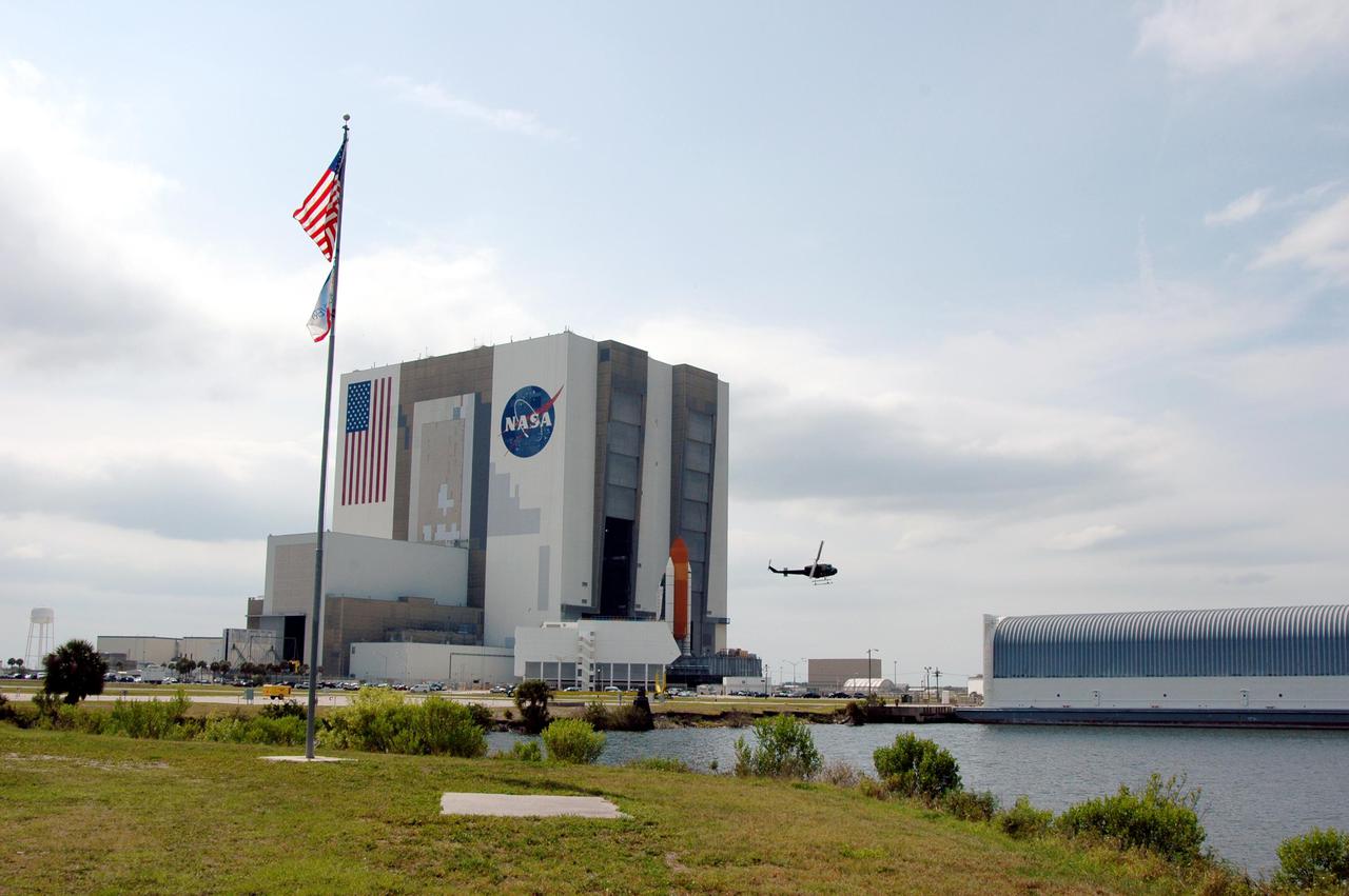KENNEDY SPACE CENTER, FLA. - Space Shuttle Discovery, atop a Mobile Launcher Platform, nears the opening to high bay 1 in the Vehicle Assembly Building (VAB) at NASA’s Kennedy Space Center. A Security helicopter hovers nearby. The view is from an area near the NASA News Center, across the Turn Basin. Docked at right is the barge that transports External Tanks from the Michoud Assembly Facility near New Orleans to Kennedy. The Shuttle is being rolled back from Launch Pad 39B. Once inside the VAB, Discovery will be demated from its External Tank and lifted into the transfer aisle. On or about June 7, Discovery will be lifted and attached to its new tank and Solid Rocket Boosters, which are already in the VAB. Only the 15th rollback in Space Shuttle Program history, the 4.2-mile journey allows additional modifications to be made to the External Tank prior to a safe Return to Flight. Discovery is expected to be rolled back to the launch pad in mid-June for Return to Flight mission STS-114. The launch window extends from July 13 to July 31.