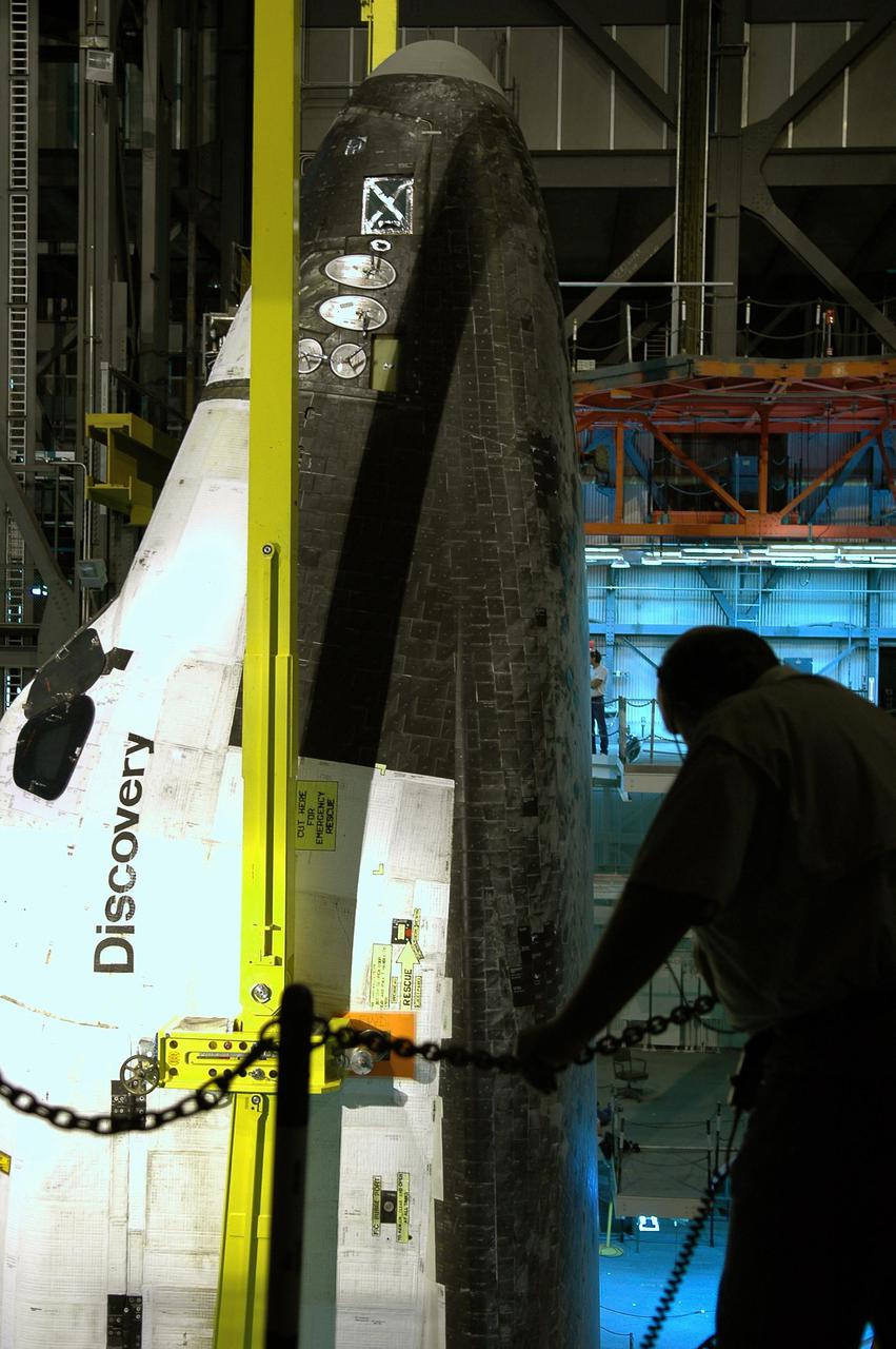 KENNEDY SPACE CENTER, FLA.  - The crane lifting orbiter Discovery casts an arc shadow across the underside of the nose as a silhouetted worker at right watches.  The orbiter, in high bay 1 of the Vehicle Assembly Building at NASA’s Kennedy Space Center, is being lifted away from the External Tank and Solid Rocket Boosters.  After demating from its External Tank (ET), the orbiter will be placed on a transporter in the transfer aisle and moved to high bay 3 for remating with another tank, ET-121.  Discovery is expected to be rolled back to the launch pad in mid-June for Return to Flight mission STS-114.  The launch window extends from July 13 to July 31.