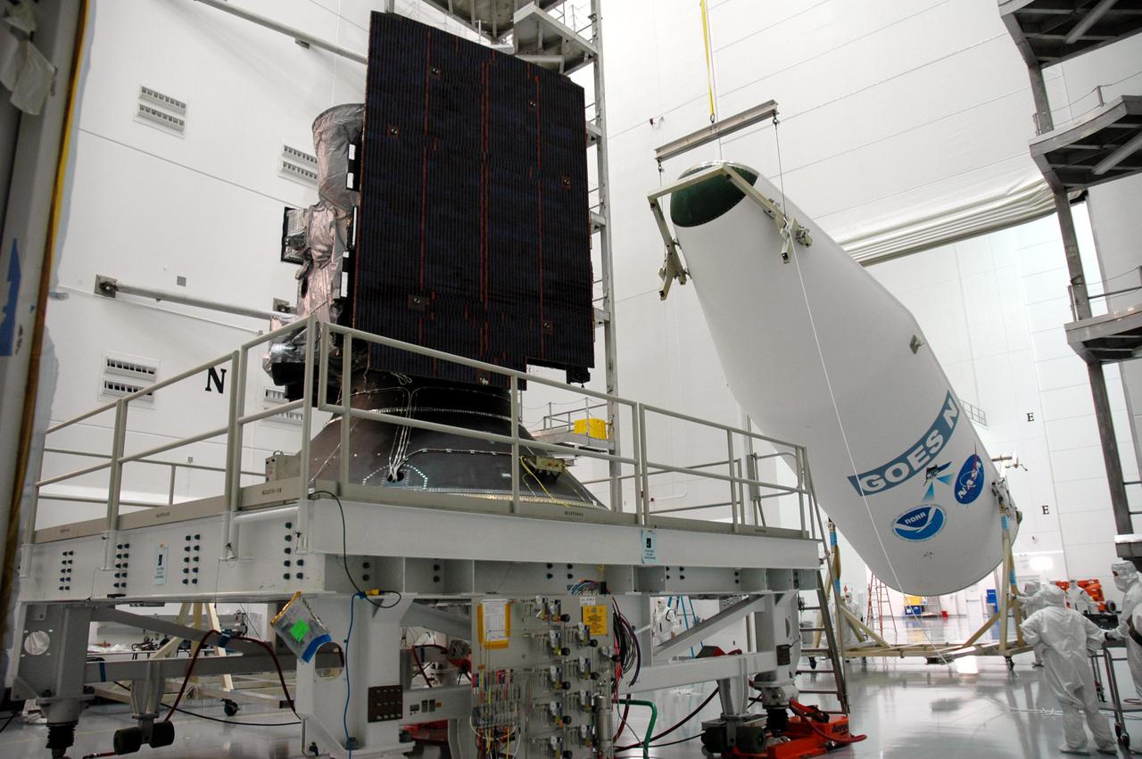 KENNEDY SPACE CENTER, FLA. - At Astrotech Space Operations in Titusville, Fla., one half of the fairing is lifted in order to install it around the GOES-N spacecraft (center). The fairing protects the spacecraft during launch. Geostationary Operational Environmental Satellites (GOES) are sponsored by NASA’s Goddard Space Flight Center and the National Oceanic and Atmospheric Administration. GOES-N is targeted to launch June 23 from Launch Complex 37 at Cape Canaveral Air Force Station in Florida.