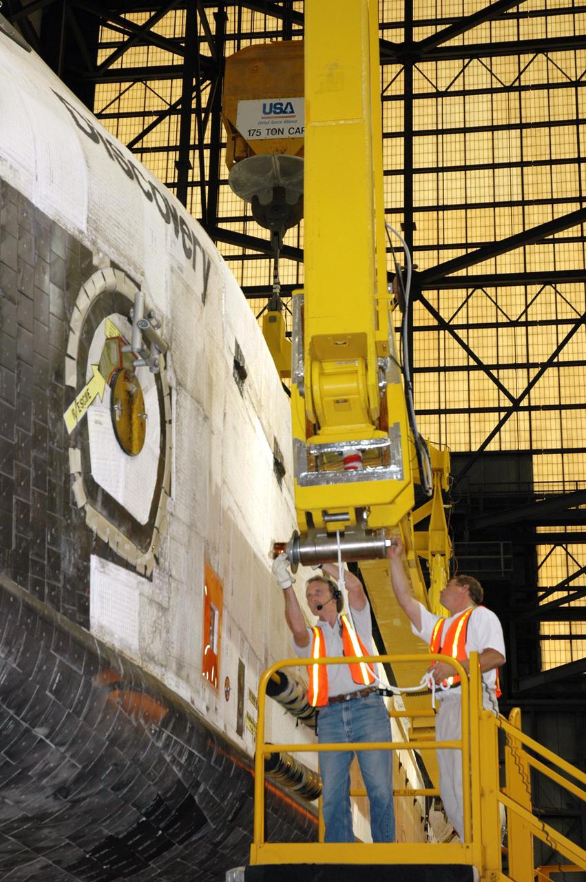 KENNEDY SPACE CENTER, FLA.  -   In the transfer aisle of the Vehicle Assembly Building, workers attach the 175-ton bridge crane to the orbiter Discovery, which is resting on an orbiter transporter.  The crane will lift Discovery to vertical for the remate to a new External Tank, ET-121. The new tank and Solid Rocket Boosters are waiting in high bay 3.  Discovery is expected roll back to the launch pad June 13 for Return to Flight mission STS-114.  The launch window extends from July 13 to July 31.