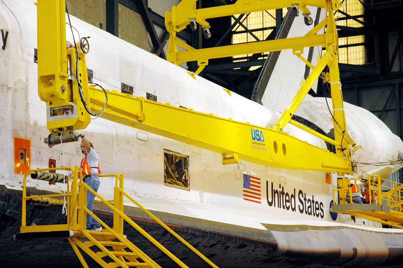KENNEDY SPACE CENTER, FLA. - In the transfer aisle of the Vehicle Assembly Building, workers attach the 175-ton bridge crane to the orbiter Discovery, which is resting on an orbiter transporter. The crane will lift Discovery to vertical for the remate to a new External Tank, ET-121. The new tank and Solid Rocket Boosters are waiting in high bay 3. Discovery is expected roll back to the launch pad June 13 for Return to Flight mission STS-114. The launch window extends from July 13 to July 31.