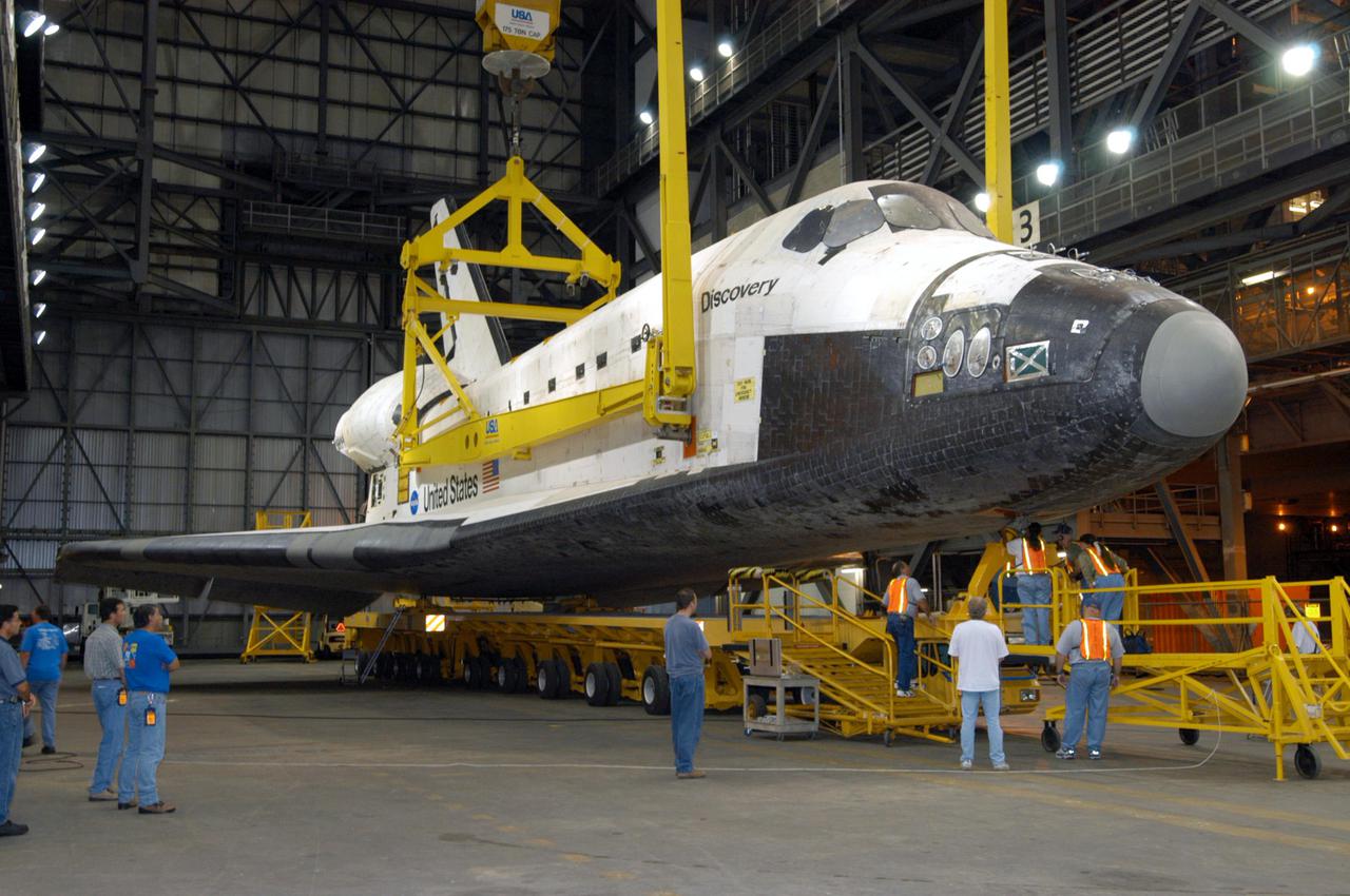 KENNEDY SPACE CENTER, FLA.  -   In the transfer aisle of the Vehicle Assembly Building, workers check under the nose of the orbiter Discovery as the 175-ton bridge crane slowly lifts Discovery off the orbiter transporter.  Discovery is being lifted to vertical for the remate with the new External Tank, ET-121, and Solid Rocket Boosters in high bay 3.  That tank was originally scheduled to fly with Atlantis on the second Return to Flight mission, STS-121. A new heater was added to the tank's feedline bellows, part of the pipeline that carries the liquid oxygen to the orbiter’s main engines, to minimize the potential for ice and frost buildup.  After the remate, technicians will work final closeouts on the fully assembled Space Shuttle stack, and perform liquid oxygen and liquid hydrogen electrical mates and an interface verification test. Discovery is currently scheduled to return to Launch Pad 39B on June 13.