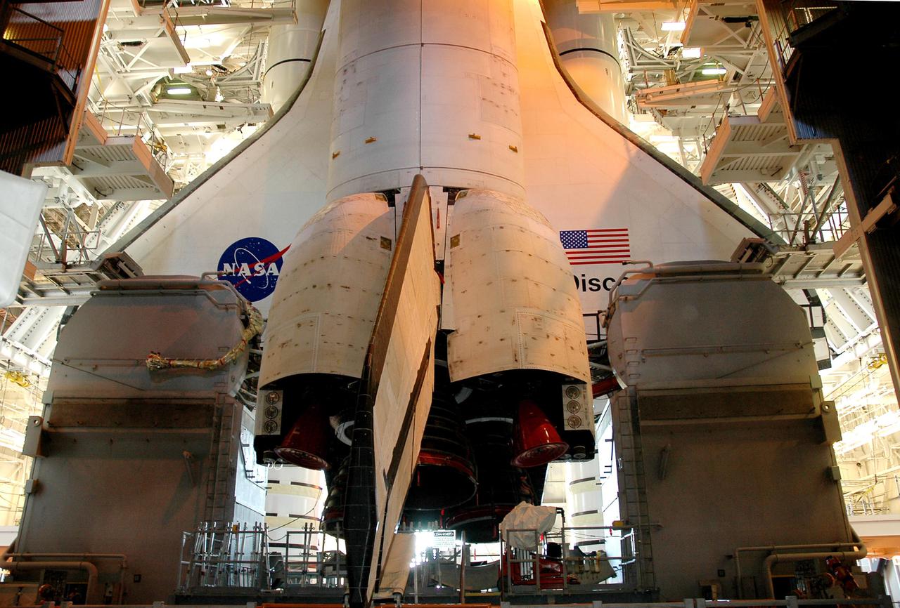 KENNEDY SPACE CENTER, FLA.  -  Lights inside the Vehicle Assembly Building cast an orange glow on Space Shuttle Discovery as waits on top of the Mobile Launcher Platform for rollout to Launch Pad 39B.  Rollout is expected to begin about 12:01 a.m. June 15 for the 4-mile, 6-hour trip to the pad. On either side of Discovery’s tail and orbital maneuvering system pods are the Tail Masts that support the fluid, gas and electrical requirements of the orbiter’s liquid oxygen and liquid hydrogen aft T-0 umbilicals. Space Shuttle Discovery's Return to Flight mission STS-114 is scheduled for liftoff in a window extending from July 13 to July 31.