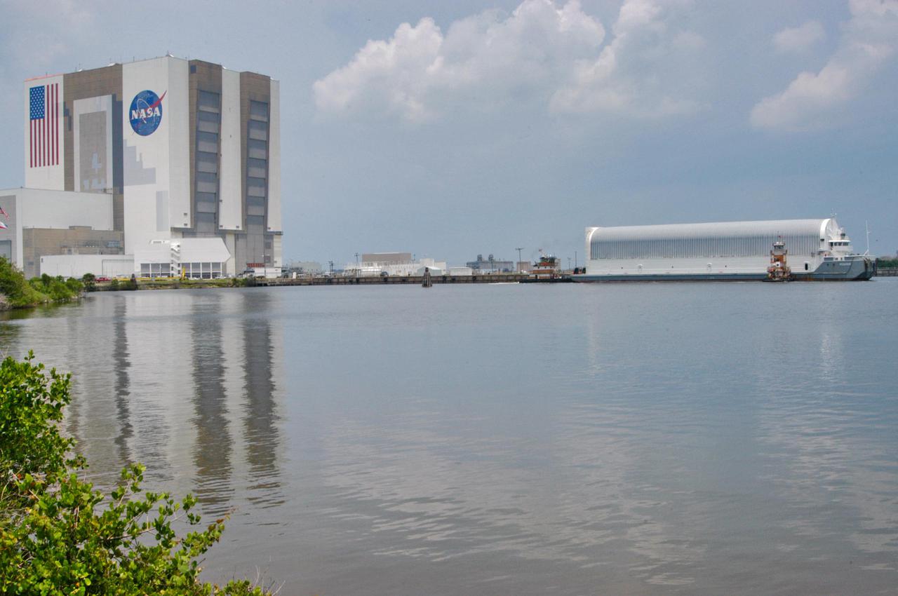 KENNEDY SPACE CENTER, FLA. - At the Turn Basin in the Launch Complex 39 Area, tug boats maneuver the barge carrying a new External Tank (ET) toward the dock. At left is the Vehicle Assembly Building, which will receive the tank after it is offloaded. The barge was towed on a 900-mile journey at sea from the Michoud Assembly Facility in New Orleans by one of NASA’s Solid Rocket Booster Retrieval Ships.