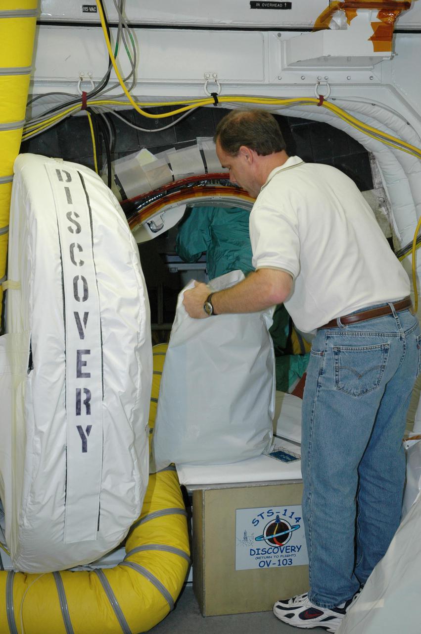 KENNEDY SPACE CENTER, FLA. - At Launch Pad 39B, United Space Alliance Flight Crew Systems engineer John Biegert uncovers a sleep restraint to be installed inside Space Shuttle Discovery, a final step in launch preparations. Launch of Discovery on its Return to Flight mission STS-114 is set for July 13, just days away. During its 12-day mission, Discovery’s seven-person crew will test new hardware and techniques to improve Shuttle safety, as well as deliver supplies to the International Space Station. Discovery’s payloads include the Multi-Purpose Logistics Module Raffaello, the Lightweight Multi-Purpose Experiment Support Structure Carrier (LMC), and the External Stowage Platform-2 (ESP-2). Raffaello will deliver supplies to the International Space Station including food, clothing and research equipment. The LMC will carry a replacement Control Moment Gyroscope and a tile repair sample box. The ESP-2 is outfitted with replacement parts.