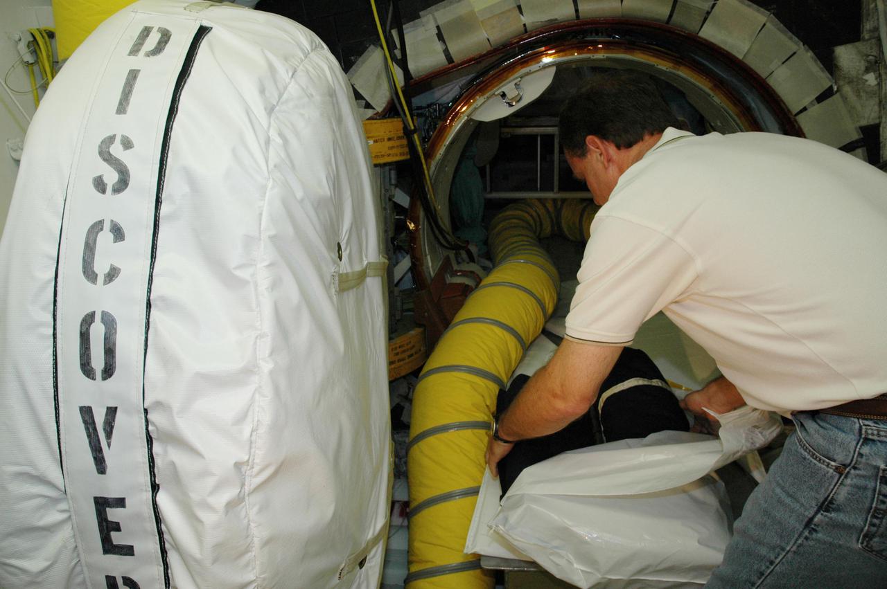 KENNEDY SPACE CENTER, FLA. - At Launch Pad 39B, United Space Alliance Flight Crew Systems engineer John Biegert passes a sleep restraint to a technician inside Space Shuttle Discovery for installation, a final step in launch preparations. Launch of Discovery on its Return to Flight mission STS-114 is set for July 13, just days away. During its 12-day mission, Discovery’s seven-person crew will test new hardware and techniques to improve Shuttle safety, as well as deliver supplies to the International Space Station. Discovery’s payloads include the Multi-Purpose Logistics Module Raffaello, the Lightweight Multi-Purpose Experiment Support Structure Carrier (LMC), and the External Stowage Platform-2 (ESP-2). Raffaello will deliver supplies to the International Space Station including food, clothing and research equipment. The LMC will carry a replacement Control Moment Gyroscope and a tile repair sample box. The ESP-2 is outfitted with replacement parts.