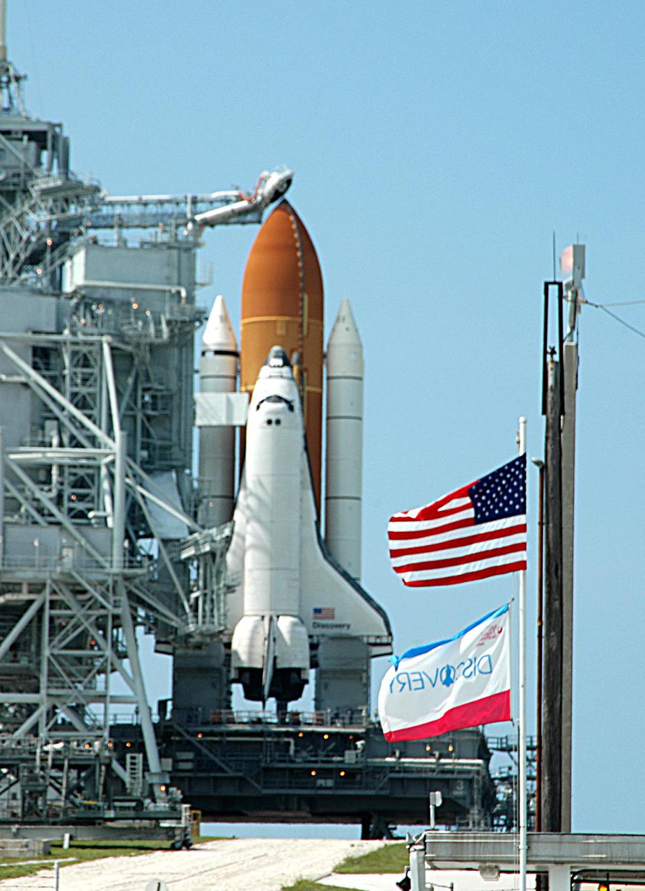 KENNEDY SPACE CENTER, FLA. - Flags are flying on Launch Pad 39B at NASA Kennedy Space Center as Space Shuttle Discovery is ready on the pad for launch after rollback of the Rotating Service Structure.  Visible above the External Tank is the gaseous oxygen vent arm (beanie cap).  Rollback of the RSS is a major preflight milestone, typically occurring during the T-11-hour hold on L-1 (the day before launch). Discovery is scheduled to lift off on the historic Return to Flight mission STS-114 at 10:39 a.m. EDT July 26 with a crew of seven.  On the mission to the International Space Station the crew will perform inspections on orbit for the first time of all of the Reinforced Carbon-Carbon (RCC) panels on the leading edge of the wings and the Thermal Protection System tiles using the new Canadian-built Orbiter Boom Sensor System and the data from 176 impact and temperature sensors. Mission Specialists will also practice repair techniques on RCC and tile samples during a spacewalk in the payload bay.  During two additional spacewalks, the crew will install the External Stowage Platform-2, equipped with spare part assemblies, and a replacement Control Moment Gyroscope contained in the Lightweight Multi-Purpose Experiment Support Structure.