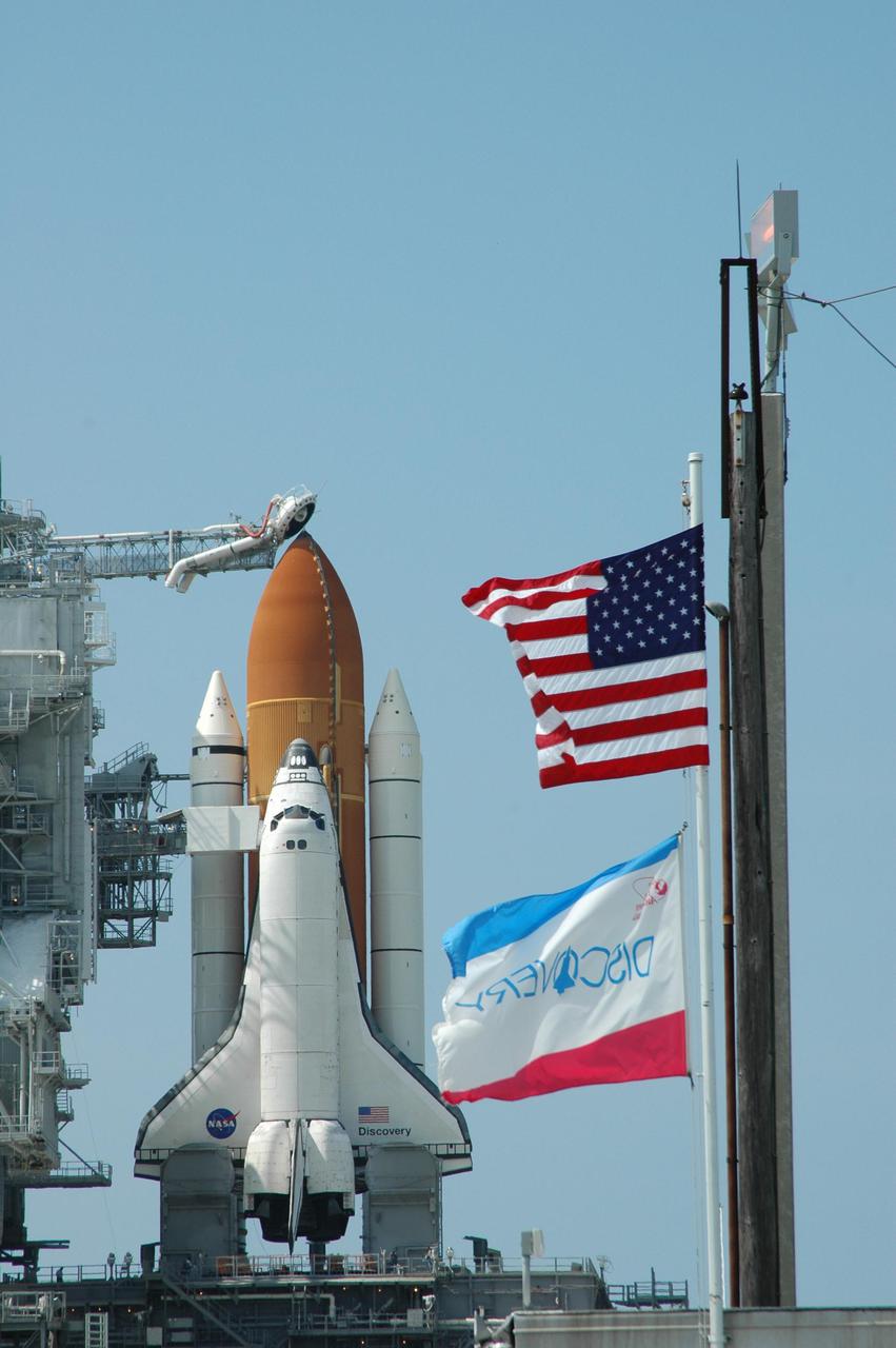 KENNEDY SPACE CENTER, FLA. - Flags are flying on Launch Pad 39B at NASA Kennedy Space Center as Space Shuttle Discovery is ready on the pad for launch after rollback of the Rotating Service Structure.  Visible above the External Tank is the gaseous oxygen vent arm (beanie cap).  Rollback of the RSS is a major preflight milestone, typically occurring during the T-11-hour hold on L-1 (the day before launch). Discovery is scheduled to lift off on the historic Return to Flight mission STS-114 at 10:39 a.m. EDT July 26 with a crew of seven.  On the mission to the International Space Station the crew will perform inspections on orbit for the first time of all of the Reinforced Carbon-Carbon (RCC) panels on the leading edge of the wings and the Thermal Protection System tiles using the new Canadian-built Orbiter Boom Sensor System and the data from 176 impact and temperature sensors. Mission Specialists will also practice repair techniques on RCC and tile samples during a spacewalk in the payload bay.  During two additional spacewalks, the crew will install the External Stowage Platform-2, equipped with spare part assemblies, and a replacement Control Moment Gyroscope contained in the Lightweight Multi-Purpose Experiment Support Structure.