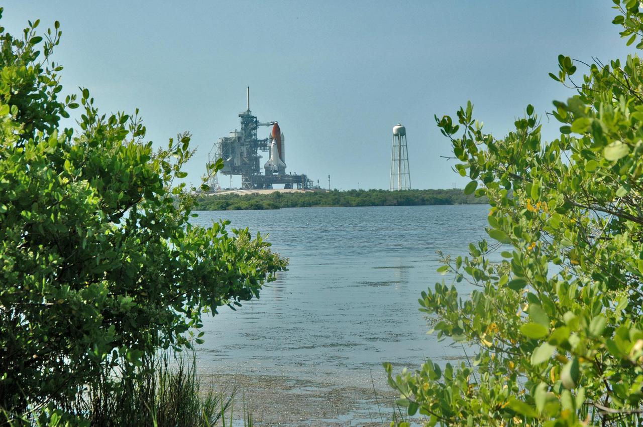 KENNEDY SPACE CENTER, FLA. - Seen after rollback of the Rotating Service Structure, and framed by marsh greenery, a fully revealed Space Shuttle Discovery on NASA Kennedy Space Center’s Launch Pad 39B erupts on the horizon beyond the pond.  Discovery is scheduled to lift off on the historic Return to Flight mission STS-114 at 10:39 a.m. EDT July 26 with a crew of seven.  On the mission to the International Space Station the crew will perform inspections on orbit for the first time of all of the Reinforced Carbon-Carbon (RCC) panels on the leading edge of the wings and the Thermal Protection System tiles using the new Canadian-built Orbiter Boom Sensor System and the data from 176 impact and temperature sensors. Mission Specialists will also practice repair techniques on RCC and tile samples during a spacewalk in the payload bay.  During two additional spacewalks, the crew will install the External Stowage Platform-2, equipped with spare part assemblies, and a replacement Control Moment Gyroscope contained in the Lightweight Multi-Purpose Experiment Support Structure.