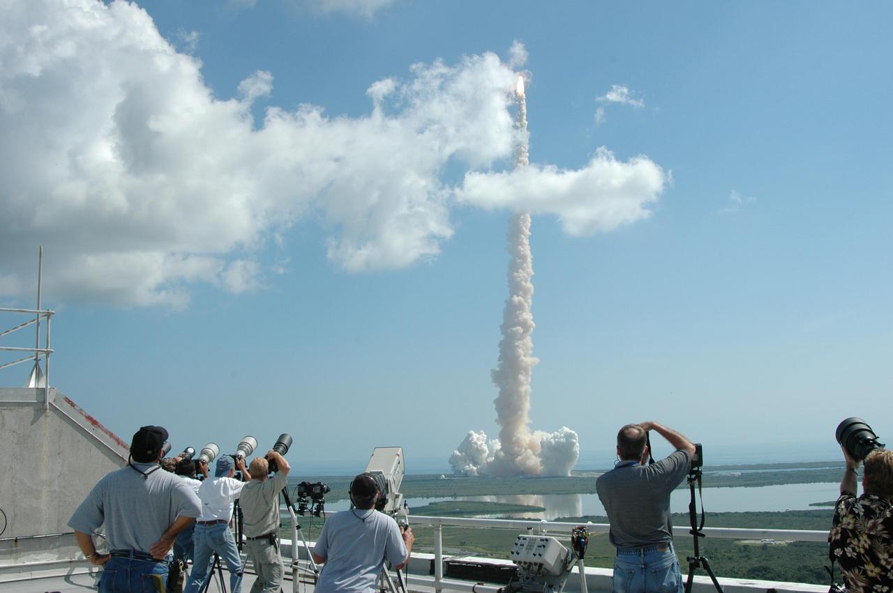 KENNEDY SPACE CENTER, FLA. - Spectators at the NASA News Center at Kennedy Space Center get a birds-eye-view of Space Shuttle Discovery as it roars through a stray cloud after liftoff at 10:39 a.m. EDT from NASA Kennedy Space Center’s Launch Pad 39B on the historic Return to Flight mission STS-114. It is the 114th Space Shuttle flight and the 31st for Discovery. The 12-day mission is expected to end with touchdown at the Shuttle Landing Facility on Aug. 7. On this mission to the International Space Station the crew will perform inspections on-orbit for the first time of all of the Reinforced Carbon-Carbon (RCC) panels on the leading edge of the wings and the Thermal Protection System tiles using the new Canadian-built Orbiter Boom Sensor System and the data from 176 impact and temperature sensors. Mission Specialists will also practice repair techniques on RCC and tile samples during a spacewalk in the payload bay. During two additional spacewalks, the crew will install the External Stowage Platform-2, equipped with spare part assemblies, and a replacement Control Moment Gyroscope contained in the Lightweight Multi-Purpose Experiment Support Structure.