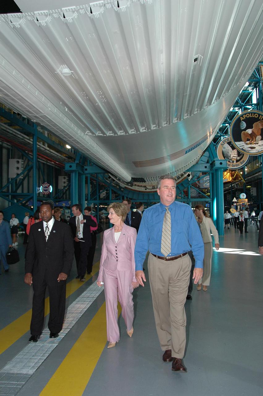KENNEDY SPACE CENTER, FLA. - At the Apollo V_Saturn Center, First Lady Laura Bush and Florida Gov. Jeb Bush stroll under the massive rocket suspended above. At left is KSC Deputy Director Woodrow Whitlow Jr. Mrs. Bush and the governor are attending the historic launch of Space Shuttle Discovery on Return to Flight mission STS-114, scheduled to lift off at 10:39 a.m. EDT from Launch Pad 39B with a crew of seven. Mrs. Bush is only the third First Lady to witness a Space Shuttle launch at KSC. On this mission to the International Space Station the crew will perform inspections on-orbit for the first time of all of the Reinforced Carbon-Carbon (RCC) panels on the leading edge of the wings and the Thermal Protection System tiles using the new Canadian-built Orbiter Boom Sensor System and the data from 176 impact and temperature sensors. Mission Specialists will also practice repair techniques on RCC and tile samples during a spacewalk in the payload bay. During two additional spacewalks, the crew will install the External Stowage Platform-2, equipped with spare part assemblies, and a replacement Control Moment Gyroscope contained in the Lightweight Multi-Purpose Experiment Support Structure. The 12-day mission is expected to end with touchdown at the Shuttle Landing Facility on Aug. 7.