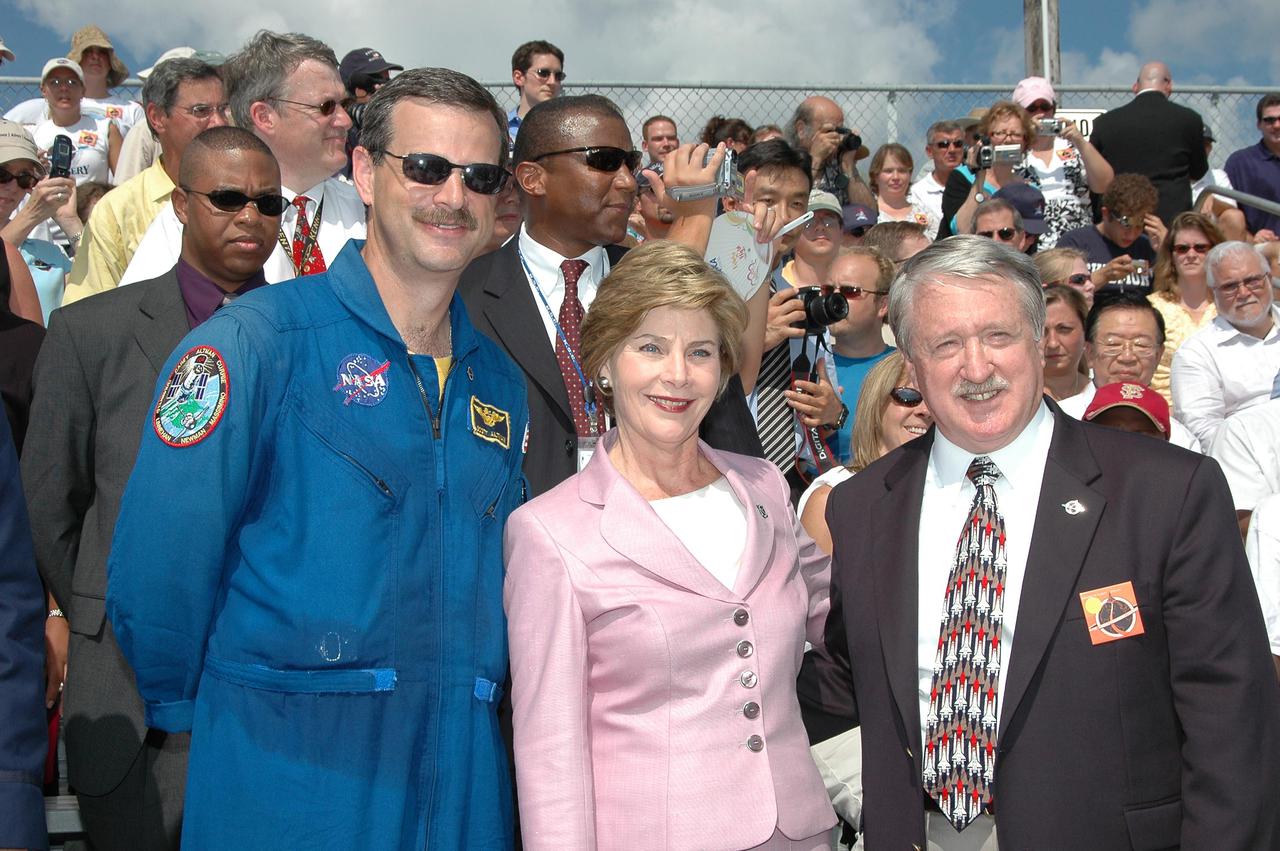 KENNEDY SPACE CENTER, FLA. - In the stands at NASA Kennedy Space Center’s Banana Creek viewing site, First Lady Laura Bush pauses for a photo with astronaut Scott Altmann and Michael O’Brien, assistant administrator for External Relations. Mrs. Bush and other guests are attending the launch of Space Shuttle Discovery on Return to Flight mission STS-114, scheduled to lift off at 10:39 a.m. EDT from Launch Pad 39B with a crew of seven. Mrs. Bush is only the third First Lady to witness a Space Shuttle launch at KSC. On this mission to the International Space Station the crew will perform inspections on-orbit for the first time of all of the Reinforced Carbon-Carbon (RCC) panels on the leading edge of the wings and the Thermal Protection System tiles using the new Canadian-built Orbiter Boom Sensor System and the data from 176 impact and temperature sensors. Mission Specialists will also practice repair techniques on RCC and tile samples during a spacewalk in the payload bay. During two additional spacewalks, the crew will install the External Stowage Platform-2, equipped with spare part assemblies, and a replacement Control Moment Gyroscope contained in the Lightweight Multi-Purpose Experiment Support Structure. The 12-day mission is expected to end with touchdown at the Shuttle Landing Facility on Aug. 7.