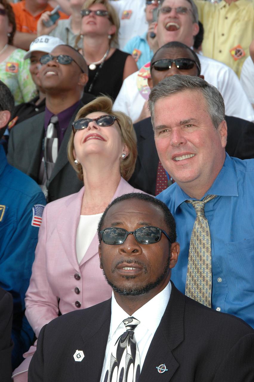 KENNEDY SPACE CENTER, FLA. - In the stands at NASA Kennedy Space Center’s Banana Creek viewing site, First Lady Laura Bush follows the path of Space Shuttle Discovery as it successfully launches on Return to Flight mission STS-114 at 10:39 a.m. EDT from Launch Pad 39B. At right is Florida Gov. Jeb Bush. KSC Deputy Director Woodrow Whitlow Jr. is in front of the governor. On this mission to the International Space Station the crew will perform inspections on-orbit for the first time of all of the Reinforced Carbon-Carbon (RCC) panels on the leading edge of the wings and the Thermal Protection System tiles using the new Canadian-built Orbiter Boom Sensor System and the data from 176 impact and temperature sensors. Mission Specialists will also practice repair techniques on RCC and tile samples during a spacewalk in the payload bay. During two additional spacewalks, the crew will install the External Stowage Platform-2, equipped with spare part assemblies, and a replacement Control Moment Gyroscope contained in the Lightweight Multi-Purpose Experiment Support Structure. The 12-day mission is expected to end with touchdown at the Shuttle Landing Facility on Aug. 7.