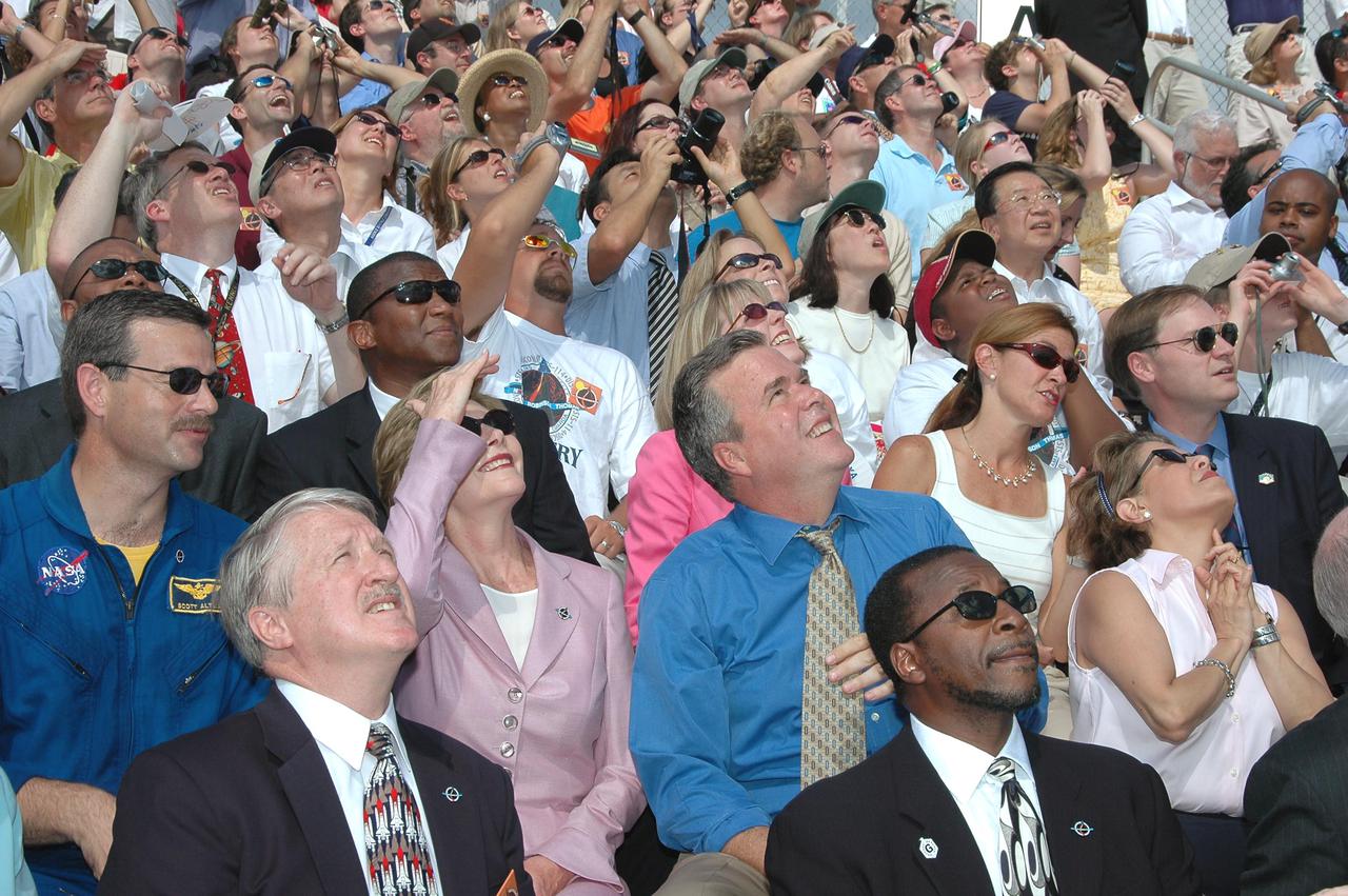 KENNEDY SPACE CENTER, FLA. - In the stands at NASA Kennedy Space Center’s Banana Creek viewing site, First Lady Laura Bush and other guests follow path of Space Shuttle Discovery as it successfully launches on Return to Flight mission STS-114 at 10:39 a.m. EDT from Launch Pad 39B. At right of Mrs. Bush is Florida Gov. Jeb Bush. KSC Deputy Director Woodrow Whitlow Jr. is in front of the governor. On this mission to the International Space Station the crew will perform inspections on-orbit for the first time of all of the Reinforced Carbon-Carbon (RCC) panels on the leading edge of the wings and the Thermal Protection System tiles using the new Canadian-built Orbiter Boom Sensor System and the data from 176 impact and temperature sensors. Mission Specialists will also practice repair techniques on RCC and tile samples during a spacewalk in the payload bay. During two additional spacewalks, the crew will install the External Stowage Platform-2, equipped with spare part assemblies, and a replacement Control Moment Gyroscope contained in the Lightweight Multi-Purpose Experiment Support Structure. The 12-day mission is expected to end with touchdown at the Shuttle Landing Facility on Aug. 7.