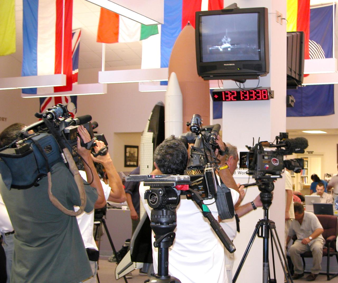 KENNEDY SPACE CENTER, FLA. - At the NASA News Center, the media turn their cameras to the television to capture the landing of Space Shuttle Discovery at Edwards Air Force Base in California. Due to weather concerns, the landing was deferred to the alternate site. The 13-day, 21-hour Return to Flight STS-114 mission ended on Runway 22 at 8:11:22 a.m. EDT with Mission Commander Eileen Collins on the controls. Discovery spent two weeks in space, where the crew demonstrated new methods to inspect and repair the Shuttle in orbit. The crew also delivered supplies, outfitted and performed maintenance on the International Space Station. A number of these tasks were conducted during three spacewalks. Photo credit: NASA_Debbie Kiger