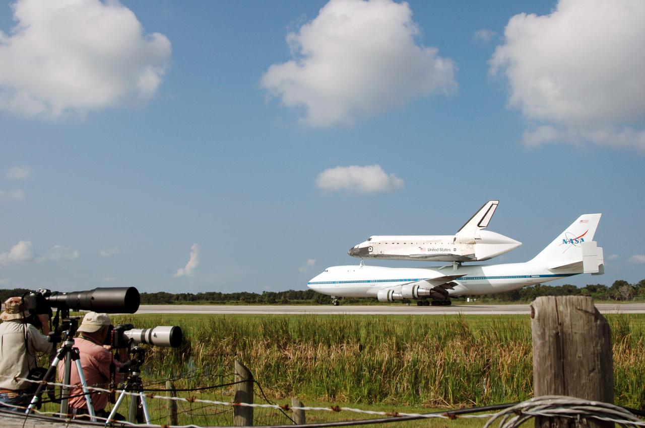 KENNEDY SPACE CENTER, FLA. - News media photographers capture the touchdown of Space Shuttle Discovery, atop a modified Boeing 747 Shuttle Carrier Aircraft (SCA), on runway 15 at NASA Kennedy Space Center's Shuttle Landing Facility (SLF) at about 10:00 a.m. EDT. The cross-country ferry flight became necessary when two days of unfavorable weather conditions at KSC forced Discovery to land on runway 22 at Edwards Air Force Base, Calif., on Aug. 9 following mission STS-114. On the return trip, stops were made at Altus Air Force Base, Okla., and Barksdale Air Force Base, La., where Discovery stayed for two nights. The SCA and Discovery will be towed to the Mate_Demate Device at the SLF where a crane will lift Discovery from the SCA and place it on solid ground. Discovery will then be towed to the Orbiter Processing Facility where preparations will begin for its next flight, STS-121.