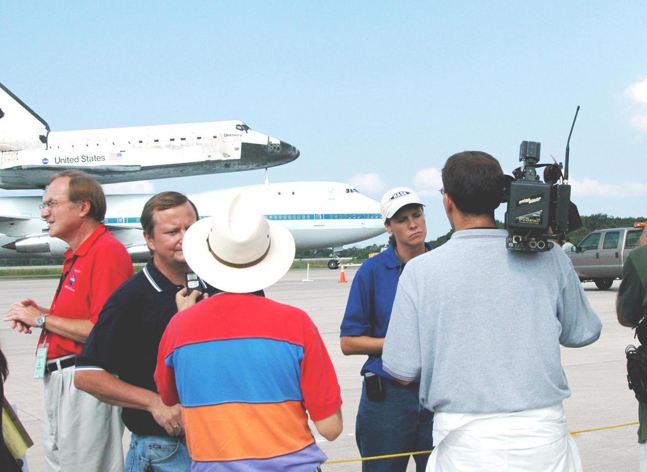 KENNEDY SPACE CENTER, FLA. -  Mike Leinbach (facing camera left), Shuttle launch director, and Stephanie Stilson (facing camera right), vehicle manager for Space Shuttle Discovery (OV-103), are interviewed by the news media at the Kennedy Space Center (KSC) Shuttle Landing Facility (SLF).  The interviews followed the touchdown of Discovery, atop a modified Boeing 747 Shuttle Carrier Aircraft (SCA), on runway 15 at the SLF at about 10:00 a.m. EDT. The cross-country ferry flight became necessary when two days of unfavorable weather conditions at KSC forced Discovery to land on runway 22 at Edwards Air Force Base, Calif., on Aug. 9 following mission STS-114. On the return trip, stops were made at Altus Air Force Base, Okla., and Barksdale Air Force Base, La., where Discovery stayed for two nights.  The SCA and Discovery will be towed to the Mate_Demate Device at the SLF where a crane will lift Discovery from the SCA and place it on solid ground. Discovery will then be towed to the Orbiter Processing Facility where preparations will begin for its next flight, STS-121.