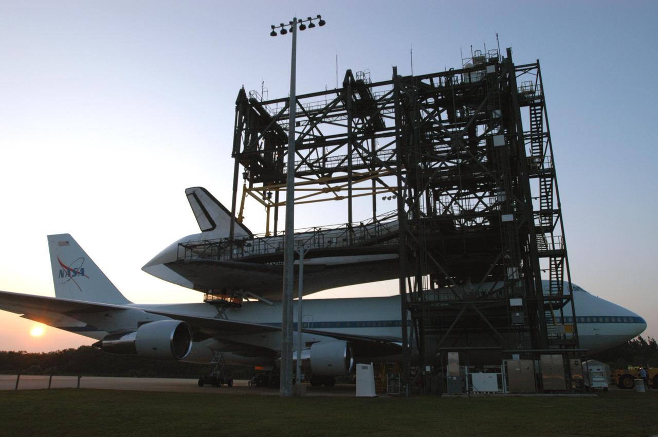 KENNEDY SPACE CENTER, FLA. -   The sun is setting behind the tail of the Shuttle Carrier Aircraft, a modified Boeing 747, and orbiter Discovery where they are parked in the mate_demate device.  Discovery was returned to Kennedy Space Center on a ferry flight from Edwards Air Force Base in California, where it landed Aug. 9 after 13 days in space on mission STS-114.  In the mate_demate device, a horizontal structure mounted at the 80-foot level between two towers controls and guides a large lift beam that attaches to the orbiter to raise and lower it.  Once Discovery is lifted off the back of the SCA, the 747 can then roll away and the orbiter will be lowered to the ground.  It will then be towed from the SLF to the Orbiter Processing Facility.  Once inside the OPF, the payload bay doors will be opened and the MPLM Raffaello brought back from the International Space Station will be unloaded and transferred to the Space Station Processing Facility.  This concludes mission STS-114.