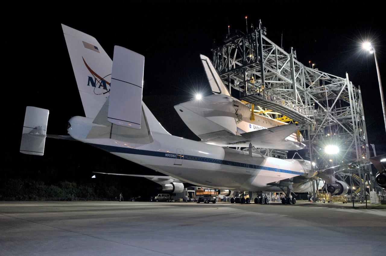 KENNEDY SPACE CENTER, FLA. - In the early morning hours at NASA Kennedy Space Center’s Shuttle Landing Facility, the orbiter Discovery is being demated from the Shuttle Carrier Aircraft, a modified Boeing 747, beneath it. Discovery was returned to Kennedy Space Center on a ferry flight from Edwards Air Force Base in California, where it landed Aug. 9 after 13 days in space on mission STS-114. In the mate_demate device, a horizontal structure mounted at the 80-foot level between two towers controls and guides a large lift beam that attaches to the orbiter to raise and lower it. Once Discovery is lifted off the back of the SCA, the 747 can then roll away and the orbiter will be lowered to the ground. It will then be towed from the SLF to the Orbiter Processing Facility. Once inside the OPF, the payload bay doors will be opened and the MPLM Raffaello brought back from the International Space Station will be unloaded and transferred to the Space Station Processing Facility. This concludes mission STS-114.