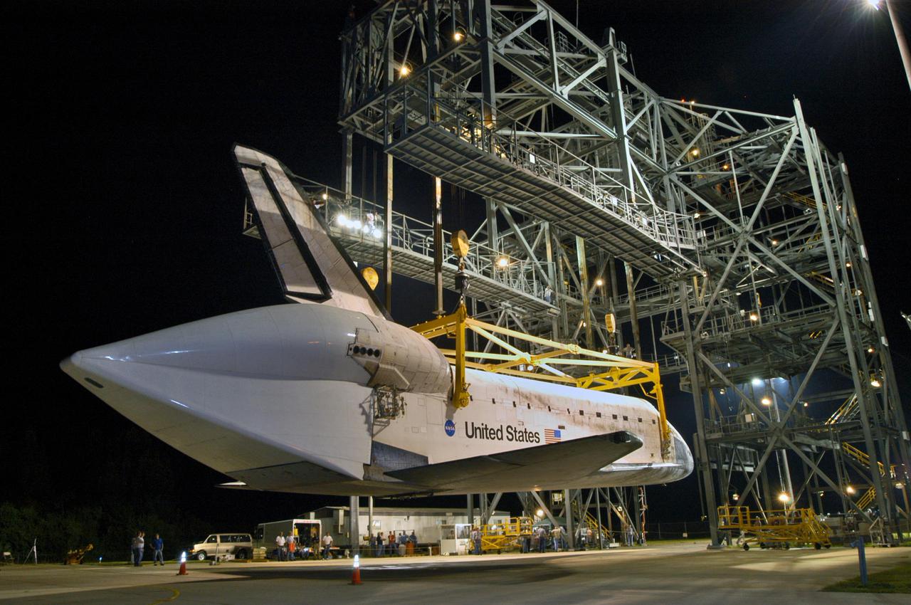 KENNEDY SPACE CENTER, FLA. -  In the early morning hours at NASA Kennedy Space Center’s Shuttle Landing Facility, the orbiter Discovery is slowly lowered toward the ground from the mate_demate device. Discovery was returned to Kennedy Space Center on a ferry flight from Edwards Air Force Base in California, where it landed Aug. 9 after 13 days in space on mission STS-114.  In the mate_demate device, a horizontal structure mounted at the 80-foot level between two towers controls and guides a large lift beam that attaches to the orbiter to raise and lower it.  The orbiter will be lowered to the ground and then be towed to the Orbiter Processing Facility.  Once inside the OPF, the payload bay doors will be opened and the MPLM Raffaello brought back from the International Space Station will be unloaded and transferred to the Space Station Processing Facility.  This concludes mission STS-114.