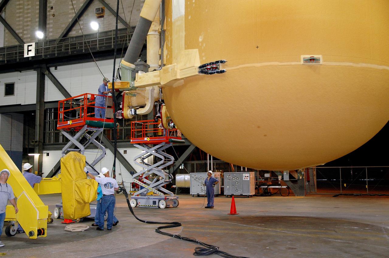 KENNEDY SPACE CENTER, FLA. - Inside NASA Kennedy Space Center’s Vehicle Assembly Building, workers secure the cranes onto External Tank 119 that enable the tank to be lowered to a horizontal position. Then it will be placed on a transporter in the transfer aisle to be moved to the barge at the Turn Basin. The tank will embark on a voyage around the Florida peninsula to the Michoud Assembly Facility in New Orleans. Delivered to KSC in June, ET-119 is the third newly redesigned tank.