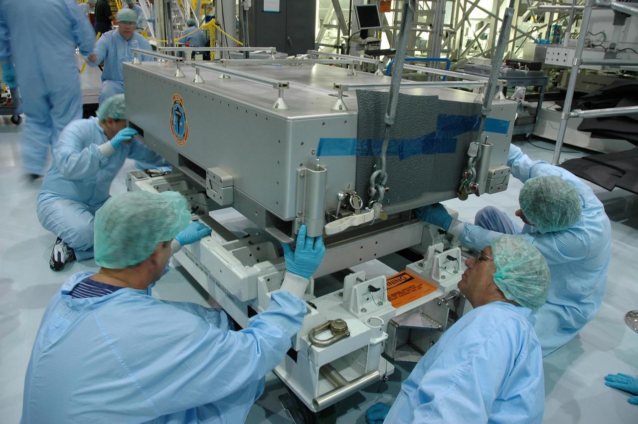 KENNEDY SPACE CENTER, FLA. - In the Space Station Processing Facility, workers ensure the tile box is secured onto a stand. The box was removed from the Lightweight Multi-Purpose Experiment Support Structure Carrier (LMC) that was returned on Space Shuttle Discovery from mission STS-114. The tile box is the Detailed Test Objective (DTO) tile sample repair kit that astronauts experimented with on the mission. The box is being returned to Johnson Space Center in Houston.