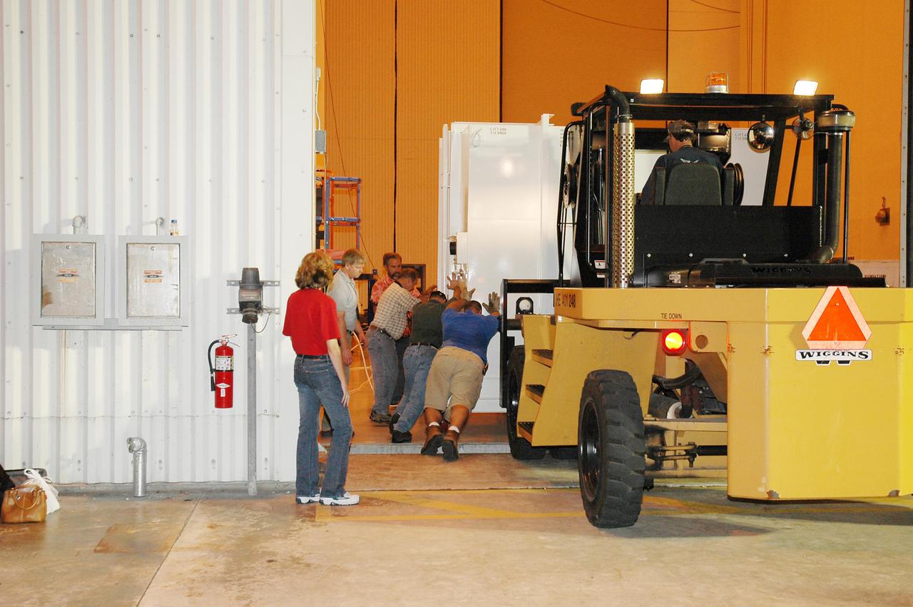 KENNEDY SPACE CENTER, FLA. - At NASA Kennedy Space Center’s Payload Hazardous Servicing Facility, human power is employed to moved the shipping container inside. The container holds the New Horizons spacecraft. New Horizons is designed to help us understand worlds at the edge of our solar system by making the first reconnaissance of Pluto and Charon - a 'double planet' and the last planet in our solar system to be visited by spacecraft. The mission will then visit one or more objects in the Kuiper Belt region beyond Neptune. New Horizons is scheduled to launch in January 2006, swing past Jupiter for a gravity boost and scientific studies in February or March 2007, and reach Pluto and its moon, Charon, in July 2015.