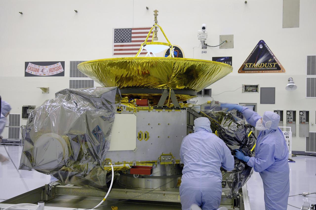 KENNEDY SPACE CENTER, FLA. - In NASA Kennedy Space Center’s Payload Hazardous Servicing Facility, workers remove the protective cover around the New Horizons spacecraft. The spacecraft will be moved to a work stand for a checkout. New Horizons will make the first reconnaissance of Pluto and Charon - a 'double planet' and the last planet in our solar system to be visited by spacecraft. The mission will then visit one or more objects in the Kuiper Belt region beyond Neptune. New Horizons is scheduled to launch in January 2006, swing past Jupiter for a gravity boost and scientific studies in February or March 2007, and reach Pluto and its moon, Charon, in July 2015.