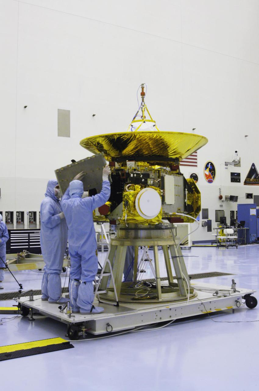 KENNEDY SPACE CENTER, FLA. - At NASA Kennedy Space Center’s Payload Hazardous Servicing Facility, technicians from the Applied Physics Laboratory hold a panel they are installing on the New Horizons spacecraft. A series of interconnecting panels will enclose the spacecraft beneath the antenna to maintain safe operating temperatures in space. New Horizons will make the first reconnaissance of Pluto and its moon, Charon - a 'double planet' and the last planet in our solar system to be visited by spacecraft. As it approaches Pluto, the spacecraft will look for ultraviolet emission from Pluto's atmosphere and make the best global maps of Pluto and Charon in green, blue, red and a special wavelength that is sensitive to methane frost on the surface. It will also take spectral maps in the near infrared, telling the science team about Pluto's and Charon's surface compositions and locations and temperatures of these materials. When the spacecraft is closest to Pluto or its moon, it will take close-up pictures in both visible and near-infrared wavelengths. The mission will then visit one or more objects in the Kuiper Belt region beyond Neptune. New Horizons is scheduled to launch in January 2006, swing past Jupiter for a gravity boost and scientific studies in February or March 2007, and reach Pluto and Charon in July 2015.