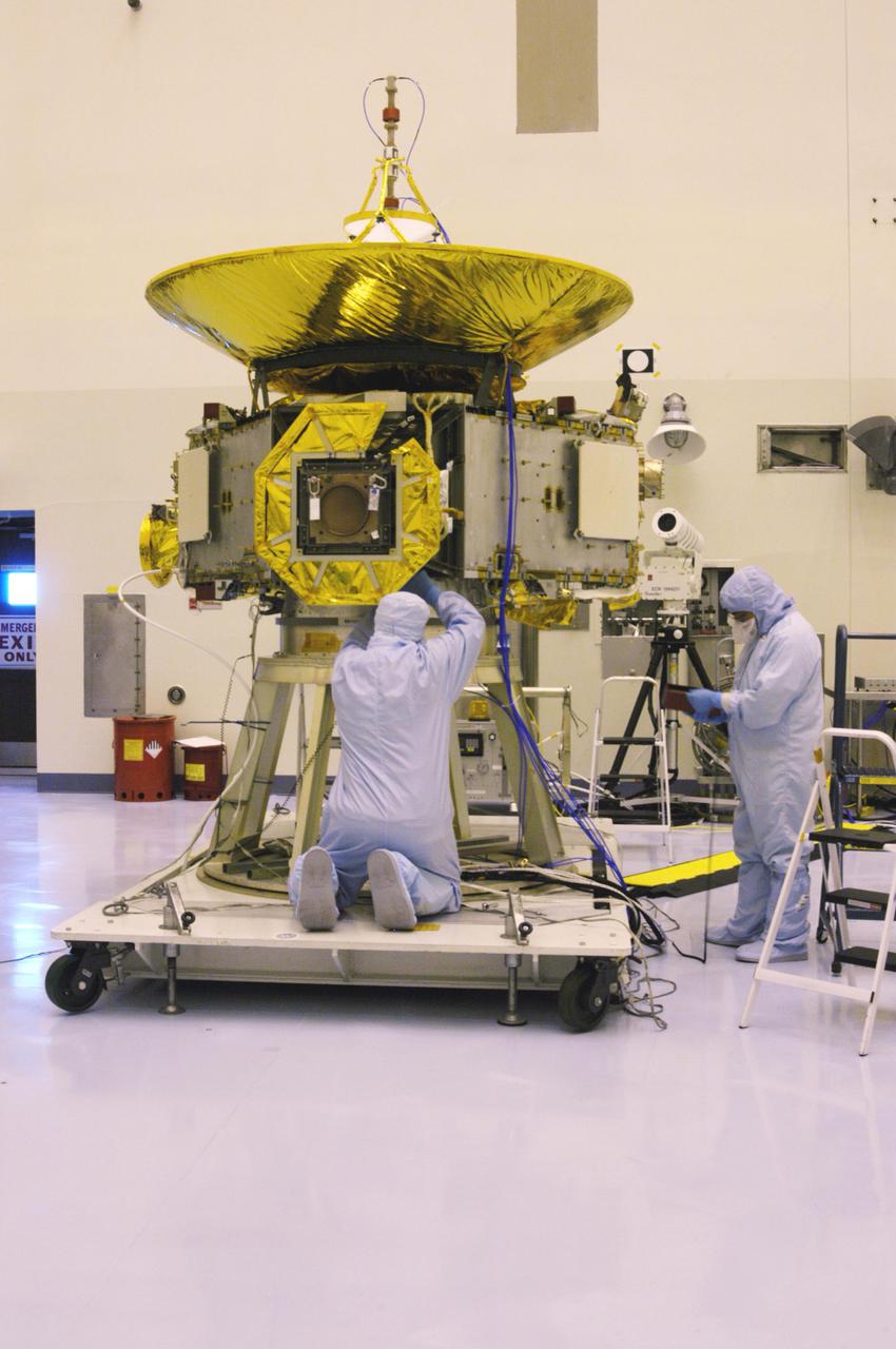 KENNEDY SPACE CENTER, FLA. - At NASA Kennedy Space Center’s Payload Hazardous Servicing Facility, technicians from the Applied Physics Laboratory work on the New Horizons spacecraft. They have been installing side panels on the spacecraft. A series of interconnecting panels will enclose the spacecraft beneath the antenna to maintain safe operating temperatures in space. New Horizons will make the first reconnaissance of Pluto and its moon, Charon - a 'double planet' and the last planet in our solar system to be visited by spacecraft. As it approaches Pluto, the spacecraft will look for ultraviolet emission from Pluto's atmosphere and make the best global maps of Pluto and Charon in green, blue, red and a special wavelength that is sensitive to methane frost on the surface. It will also take spectral maps in the near infrared, telling the science team about Pluto's and Charon's surface compositions and locations and temperatures of these materials. When the spacecraft is closest to Pluto or its moon, it will take close-up pictures in both visible and near-infrared wavelengths. The mission will then visit one or more objects in the Kuiper Belt region beyond Neptune. New Horizons is scheduled to launch in January 2006, swing past Jupiter for a gravity boost and scientific studies in February or March 2007, and reach Pluto and Charon in July 2015.
