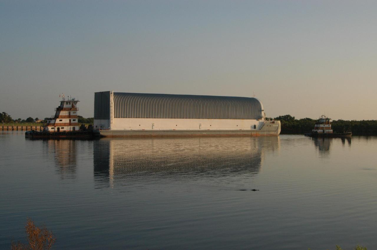 KENNEDY SPACE CENTER, FLA. -   Just after dawn, an alligator (in the foreground) watches as a tugboat pushes the Pegasus barge away from the dock at the Turn Basin in the Launch Complex 39 area.  The barge is carrying external tank 119 (ET-119) and will be towed by the solid rocket booster retrieval ship Freedom Star to NASA’s Michoud Assembly Facility near New Orleans.  Delivered to Kennedy in June, ET-119 is the third newly redesigned tank and is the only tank that contains the liquid oxygen heater.  The tank is being returned to Michoud for testing and further modifications.  ET-119 will be the tank used on return to flight mission STS-121.