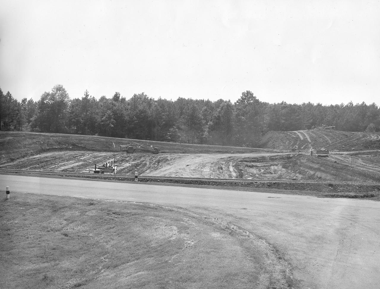 At its founding, the Marshall Space Flight Center (MSFC) inherited the Army’s Jupiter and Redstone test stands, but much larger facilities were needed for the giant stages of the Saturn V. From 1960 to 1964, the existing stands were remodeled and a sizable new test area was developed. The new comprehensive test complex for propulsion and structural dynamics was unique within the nation and the free world, and they remain so today because they were constructed with foresight to meet the future as well as on going needs. Construction of the S-IC Static test stand complex began in 1961 in the west test area of MSFC, and was completed in 1964. The S-IC static test stand was designed to develop and test the 138-ft long and 33-ft diameter Saturn V S-IC first stage, or booster stage, weighing in at 280,000 pounds. Required to hold down the brute force of a 7,500,000-pound thrust produced by 5 F-1 engines, the S-IC static test stand was designed and constructed with the strength of hundreds of tons of steel and 12,000,000 pounds of cement, planted down to bedrock 40 feet below ground level. The foundation walls, constructed with concrete and steel, are 4 feet thick. The base structure consists of four towers with 40-foot-thick walls extending upward 144 feet above ground level. The structure was topped by a crane with a 135-foot boom. With the boom in the upright position, the stand was given an overall height of 405 feet, placing it among the highest structures in Alabama at the time. In this photo, taken July 10, 1961, actual ground breaking has occurred for the S-IC test stand site. 