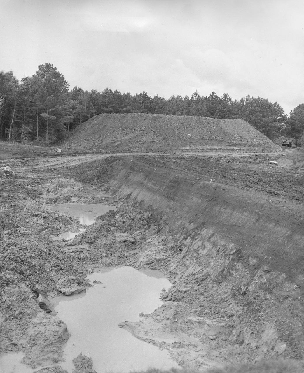At its founding, the Marshall Space Flight Center (MSFC) inherited the Army’s Jupiter and Redstone test stands, but much larger facilities were needed for the giant stages of the Saturn V. From 1960 to 1964, the existing stands were remodeled and a sizable new test area was developed. The new comprehensive test complex for propulsion and structural dynamics was unique within the nation and the free world, and they remain so today because they were constructed with foresight to meet the future as well as on going needs. Construction of the S-IC Static test stand complex began in 1961 in the west test area of MSFC, and was completed in 1964. The S-IC static test stand was designed to develop and test the 138-ft long and 33-ft diameter Saturn V S-IC first stage, or booster stage, weighing in at 280,000 pounds. Required to hold down the brute force of a 7,500,000-pound thrust produced by 5 F-1 engines, the S-IC static test stand was designed and constructed with the strength of hundreds of tons of steel and 12,000,000 pounds of cement, planted down to bedrock 40 feet below ground level. The foundation walls, constructed with concrete and steel, are 4 feet thick. The base structure consists of four towers with 40-foot-thick walls extending upward 144 feet above ground level. The structure was topped by a crane with a 135-foot boom. With the boom in the upright position, the stand was given an overall height of 405 feet, placing it among the highest structures in Alabama at the time. In this photo, taken July 13, 1961, progress is being made with the excavation of the S-IC test stand site. During the digging, a natural spring was disturbed which caused a constant flooding problem. Pumps were used to remove the water all through the construction process and the site is still pumped today.