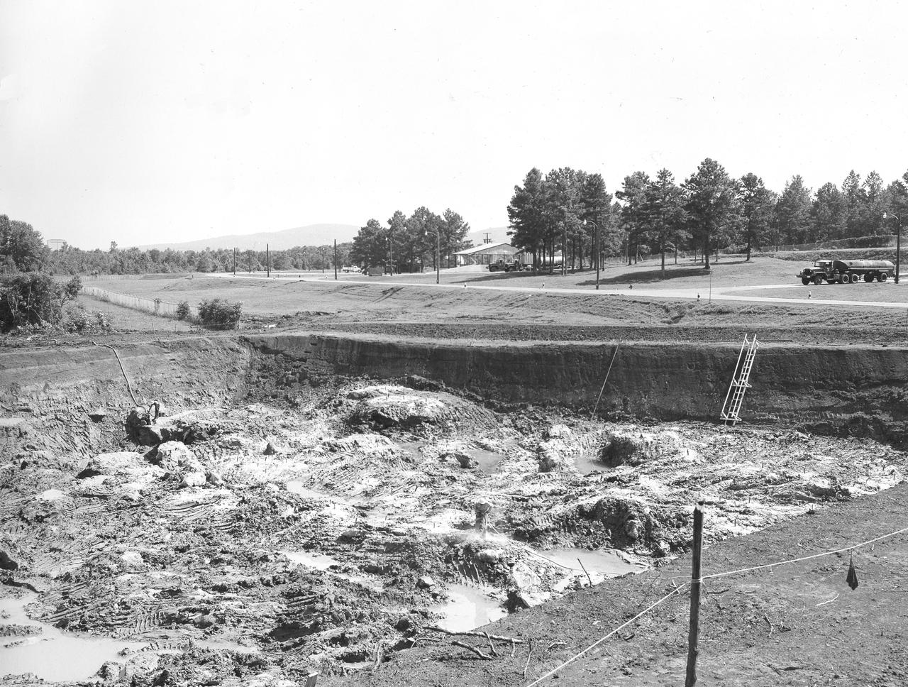 At its founding, the Marshall Space Flight Center (MSFC) inherited the Army’s Jupiter and Redstone test stands, but much larger facilities were needed for the giant stages of the Saturn V. From 1960 to 1964, the existing stands were remodeled and a sizable new test area was developed. The new comprehensive test complex for propulsion and structural dynamics was unique within the nation and the free world, and they remain so today because they were constructed with foresight to meet the future as well as on going needs. Construction of the S-IC Static test stand complex began in 1961 in the west test area of MSFC, and was completed in 1964. The S-IC static test stand was designed to develop and test the 138-ft long and 33-ft diameter Saturn V S-IC first stage, or booster stage, weighing in at 280,000 pounds. Required to hold down the brute force of a 7,500,000-pound thrust produced by 5 F-1 engines, the S-IC static test stand was designed and constructed with the strength of hundreds of tons of steel and 12,000,000 pounds of cement, planted down to bedrock 40 feet below ground level. The foundation walls, constructed with concrete and steel, are 4 feet thick. The base structure consists of four towers with 40-foot-thick walls extending upward 144 feet above ground level. The structure was topped by a crane with a 135-foot boom. With the boom in the upright position, the stand was given an overall height of 405 feet, placing it among the highest structures in Alabama at the time. In this photo, taken July 21, 1961, a worker can be seen inside the test stand work area with a jack hammer.