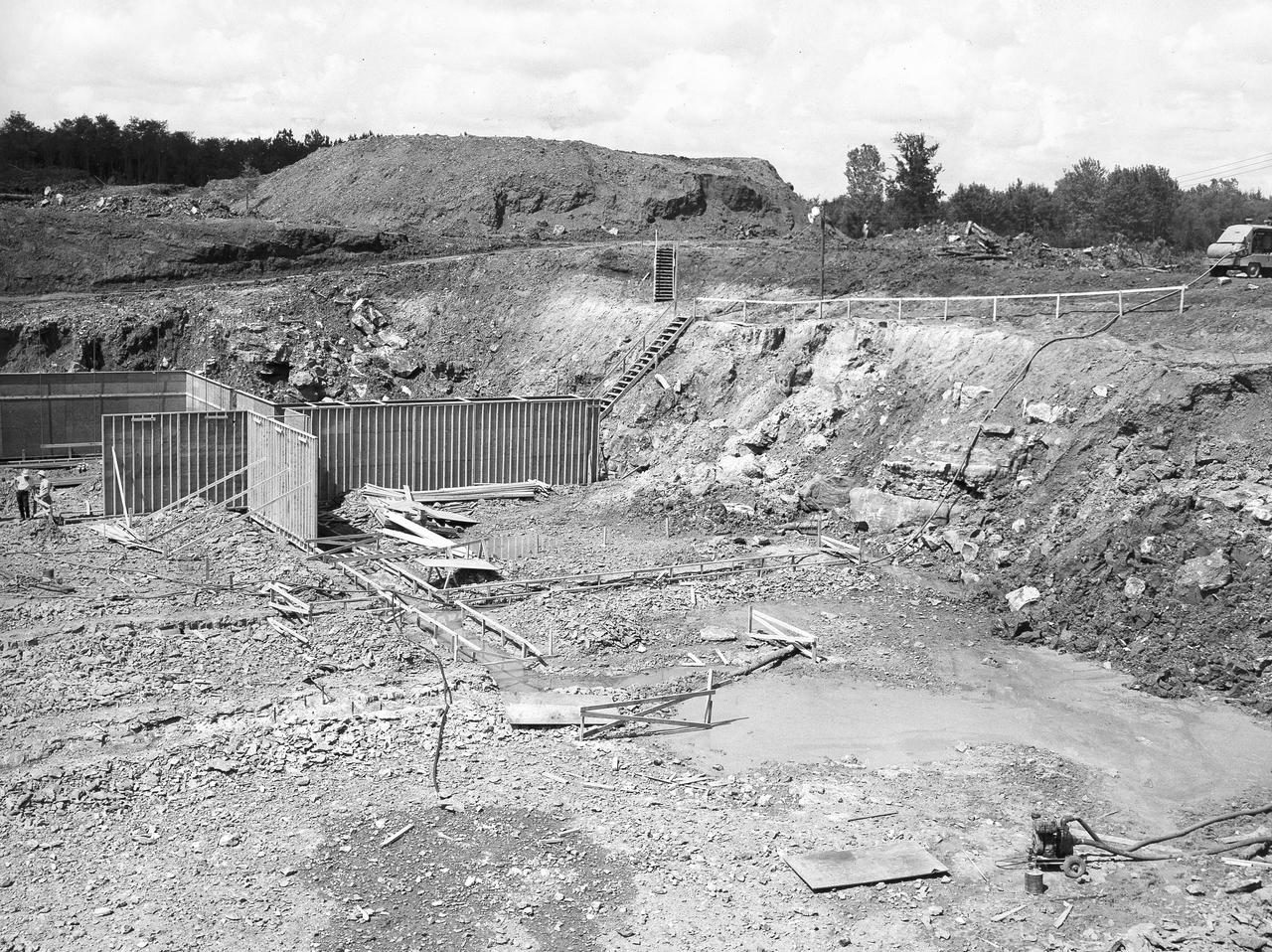 At its founding, the Marshall Space Flight Center (MSFC) inherited the Army’s Jupiter and Redstone test stands, but much larger facilities were needed for the giant stages of the Saturn V. From 1960 to 1964, the existing stands were remodeled and a sizable new test area was developed. The new comprehensive test complex for propulsion and structural dynamics was unique within the nation and the free world, and they remain so today because they were constructed with foresight to meet the future as well as on going needs. Construction of the S-IC Static test stand complex began in 1961 in the west test area of MSFC, and was completed in 1964. The S-IC static test stand was designed to develop and test the 138-ft long and 33-ft diameter Saturn V S-IC first stage, or booster stage, weighing in at 280,000 pounds. Required to hold down the brute force of a 7,500,000-pound thrust produced by 5 F-1 engines, the S-IC static test stand was designed and constructed with the strength of hundreds of tons of steel and 12,000,000 pounds of cement, planted down to bedrock 40 feet below ground level. The foundation walls, constructed with concrete and steel, are 4 feet thick. The base structure consists of four towers with 40-foot-thick walls extending upward 144 feet above ground level. The structure was topped by a crane with a 135-foot boom. With the boom in the upright position, the stand was given an overall height of 405 feet, placing it among the highest structures in Alabama at the time. This photo, taken September 5, 1961, shows the construction of forms which became the concrete foundation for the massive stand. The lower right hand corner reveals a pump used for extracting water emerging from a disturbed natural spring that occurred during excavation of the site. The pumping became a daily ritual and the site is still pumped today.