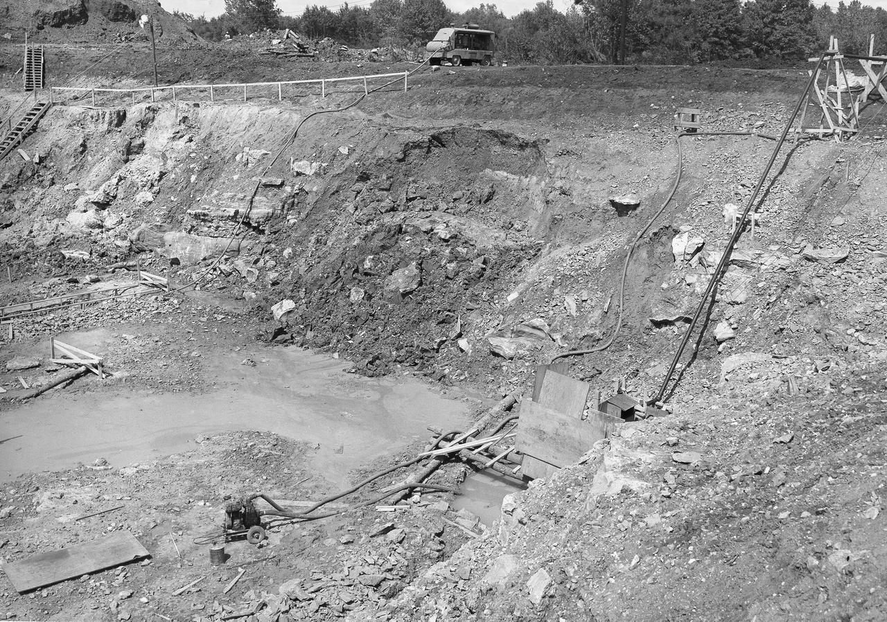 At its founding, the Marshall Space Flight Center (MSFC) inherited the Army’s Jupiter and Redstone test stands, but much larger facilities were needed for the giant stages of the Saturn V. From 1960 to 1964, the existing stands were remodeled and a sizable new test area was developed. The new comprehensive test complex for propulsion and structural dynamics was unique within the nation and the free world, and they remain so today because they were constructed with foresight to meet the future as well as on going needs. Construction of the S-IC Static test stand complex began in 1961 in the west test area of MSFC, and was completed in 1964. The S-IC static test stand was designed to develop and test the 138-ft long and 33-ft diameter Saturn V S-IC first stage, or booster stage, weighing in at 280,000 pounds. Required to hold down the brute force of a 7,500,000-pound thrust produced by 5 F-1 engines, the S-IC static test stand was designed and constructed with the strength of hundreds of tons of steel and 12,000,000 pounds of cement, planted down to bedrock 40 feet below ground level. The foundation walls, constructed with concrete and steel, are 4 feet thick. The base structure consists of four towers with 40-foot-thick walls extending upward 144 feet above ground level. The structure was topped by a crane with a 135-foot boom. With the boom in the upright position, the stand was given an overall height of 405 feet, placing it among the highest structures in Alabama at the time. This photo, taken September 5, 1961, shows pumps used for extracting water emerging form a disturbed natural spring that occurred during the excavation of the site. The pumping became a daily ritual and the site is still pumped today.