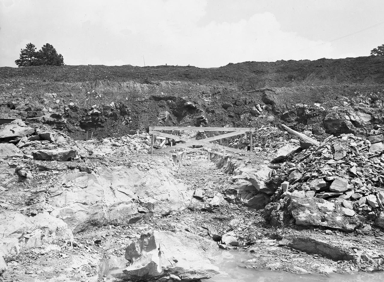 At its founding, the Marshall Space Flight Center (MSFC) inherited the Army’s Jupiter and Redstone test stands, but much larger facilities were needed for the giant stages of the Saturn V. From 1960 to 1964, the existing stands were remodeled and a sizable new test area was developed. The new comprehensive test complex for propulsion and structural dynamics was unique within the nation and the free world, and they remain so today because they were constructed with foresight to meet the future as well as on going needs. Construction of the S-IC Static test stand complex began in 1961 in the west test area of MSFC, and was completed in 1964. The S-IC static test stand was designed to develop and test the 138-ft long and 33-ft diameter Saturn V S-IC first stage, or booster stage, weighing in at 280,000 pounds. Required to hold down the brute force of a 7,500,000-pound thrust produced by 5 F-1 engines, the S-IC static test stand was designed and constructed with the strength of hundreds of tons of steel and 12,000,000 pounds of cement, planted down to bedrock 40 feet below ground level. The foundation walls, constructed with concrete and steel, are 4 feet thick. The base structure consists of four towers with 40-foot-thick walls extending upward 144 feet above ground level. The structure was topped by a crane with a 135-foot boom. With the boom in the upright position, the stand was given an overall height of 405 feet, placing it among the highest structures in Alabama at the time. This photo shows the construction progress of the S-IC test stand as of September 7, 1961.